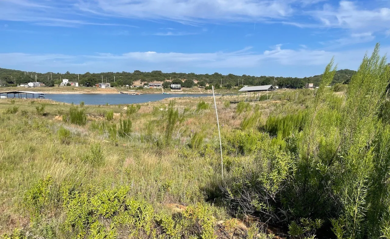 Expansive waterfront property featuring a large body of water, distant structures, and a natural, undeveloped landscape