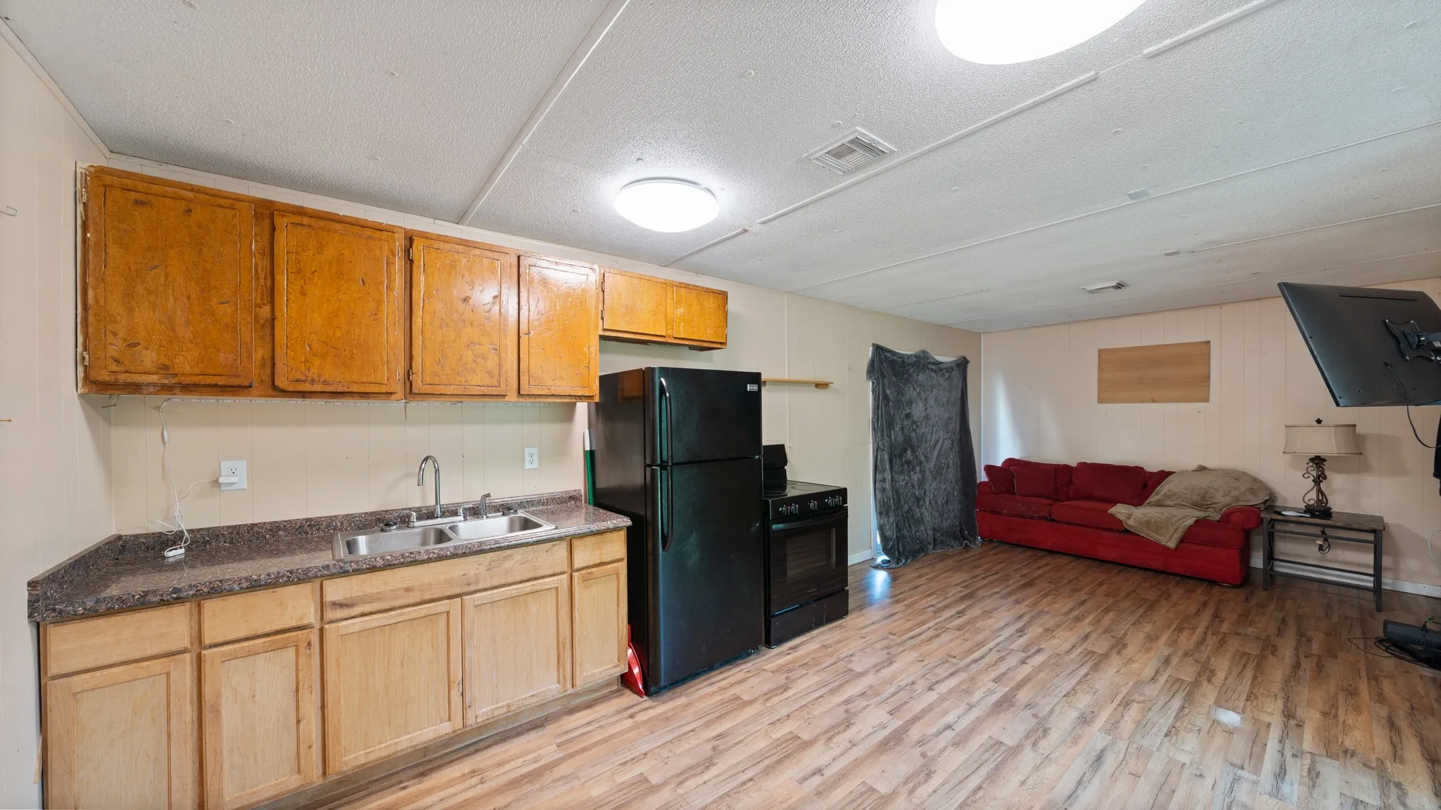 Kitchenette with wood-finish cabinetry, stainless steel sink, and dark countertops