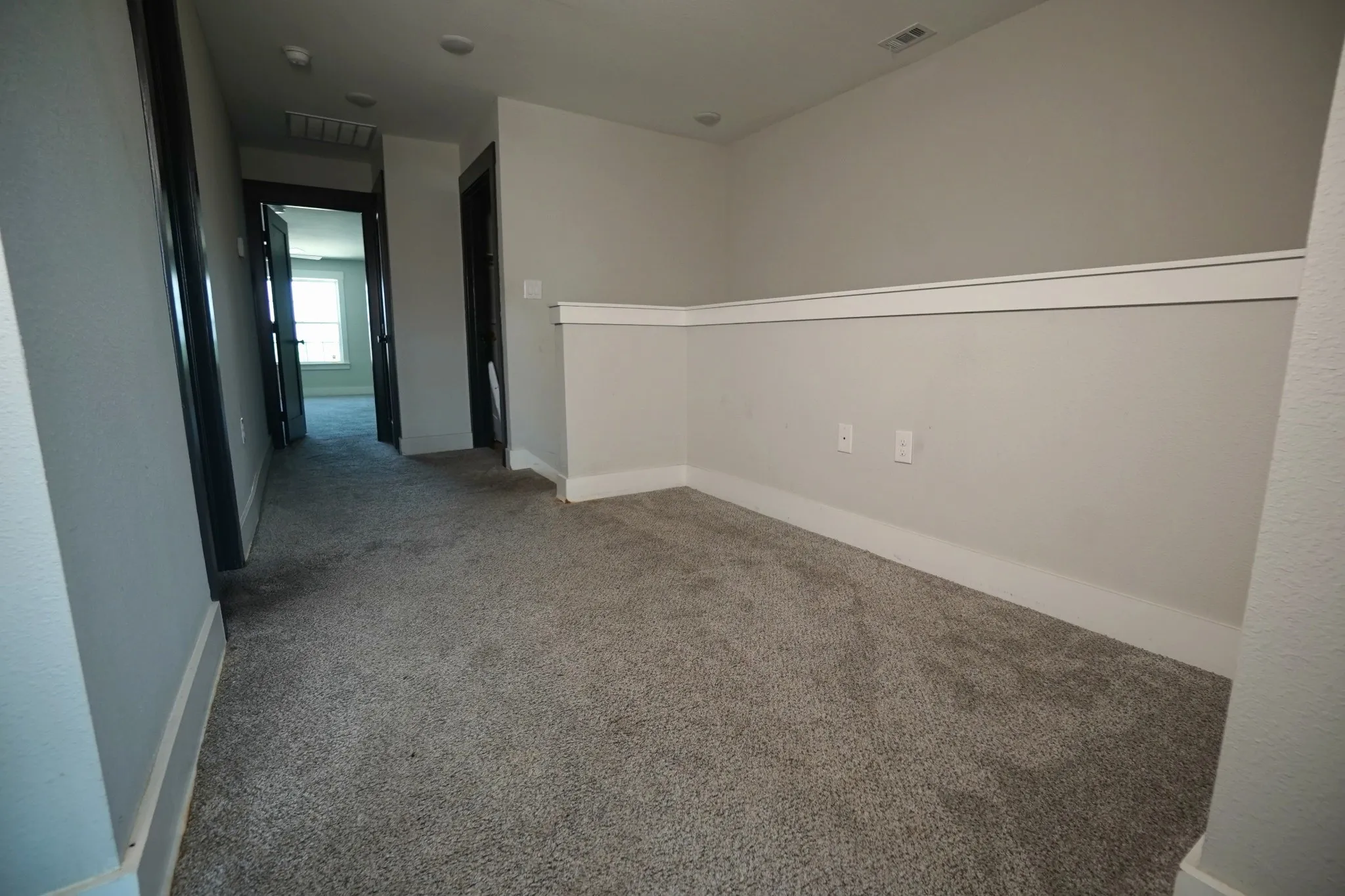 Carpeted hallway featuring light gray walls, white chair rail molding, and dark trim around doorways