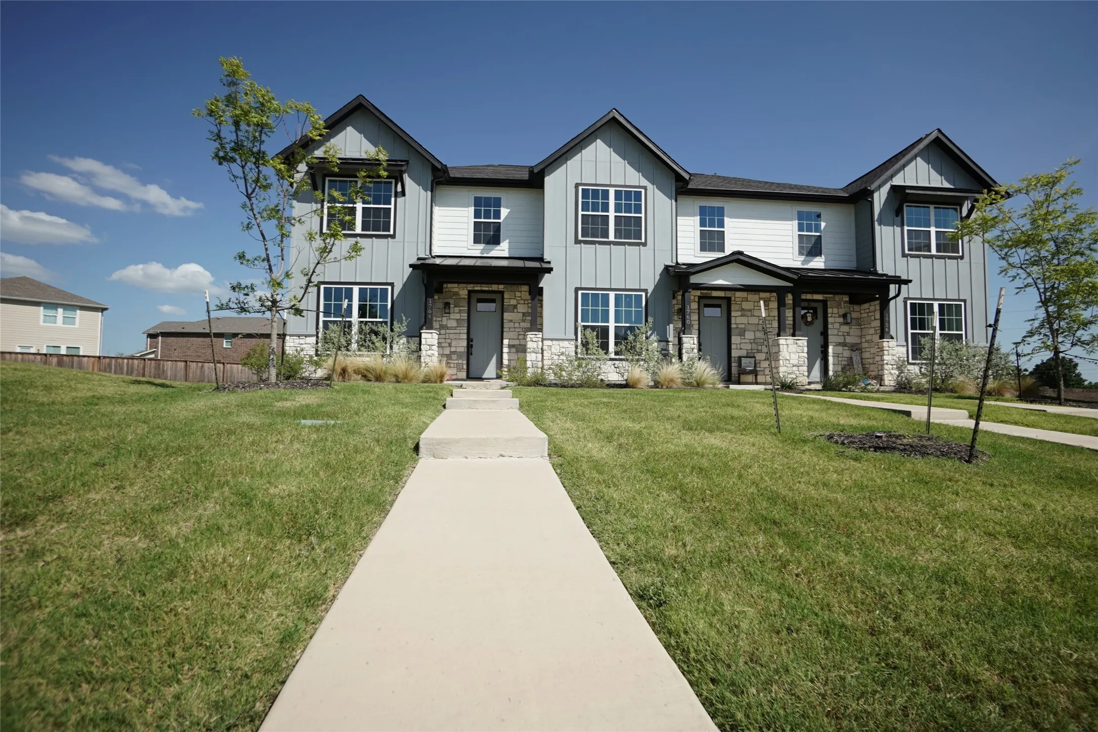 Modern townhome exterior with stone accents, vertical and horizontal siding, multiple windows, and a covered entry