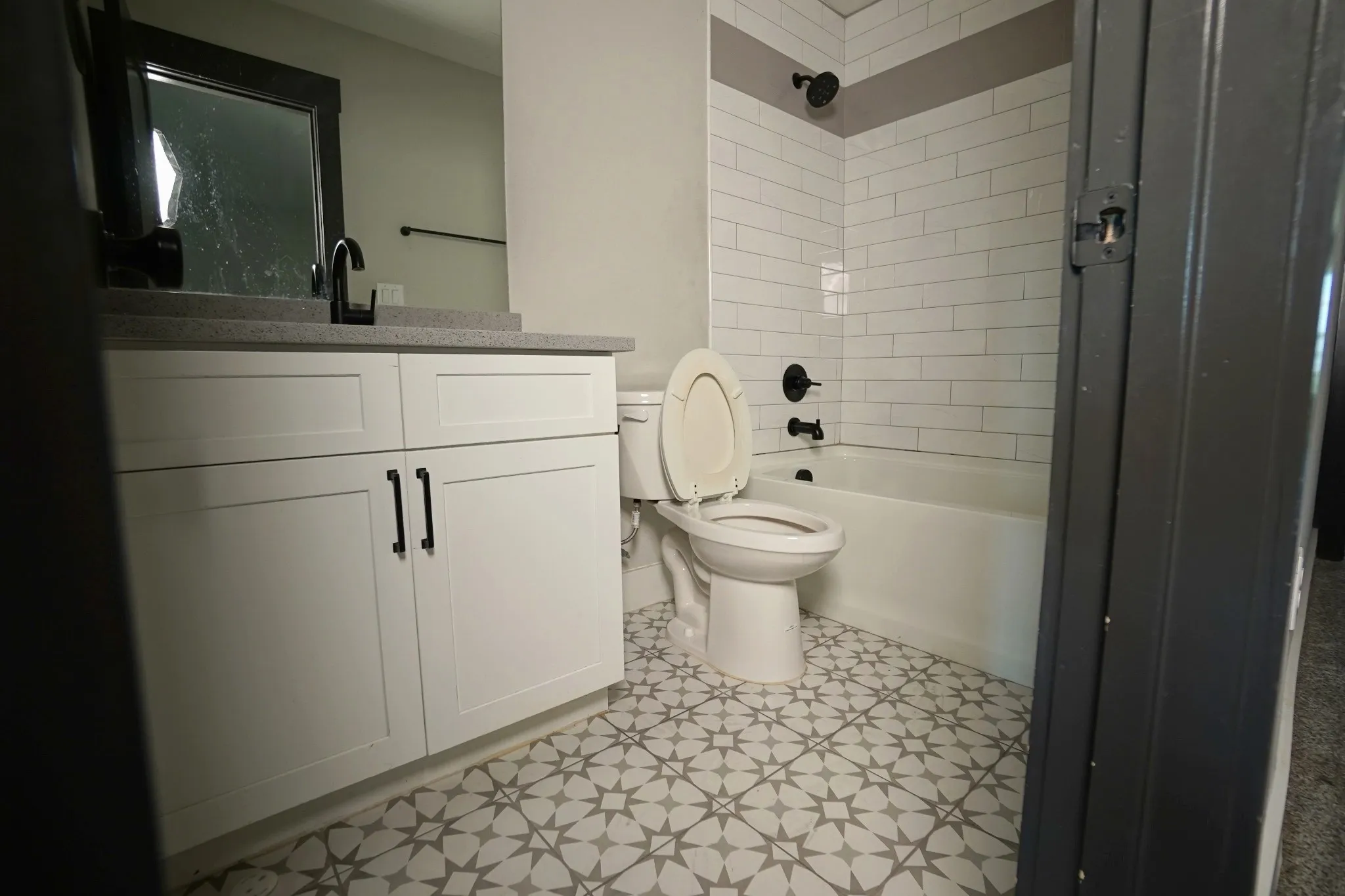 Modern bathroom featuring decorative floor tiles, a white vanity with dark hardware, a coordinated dark faucet, and subway tile shower surround
