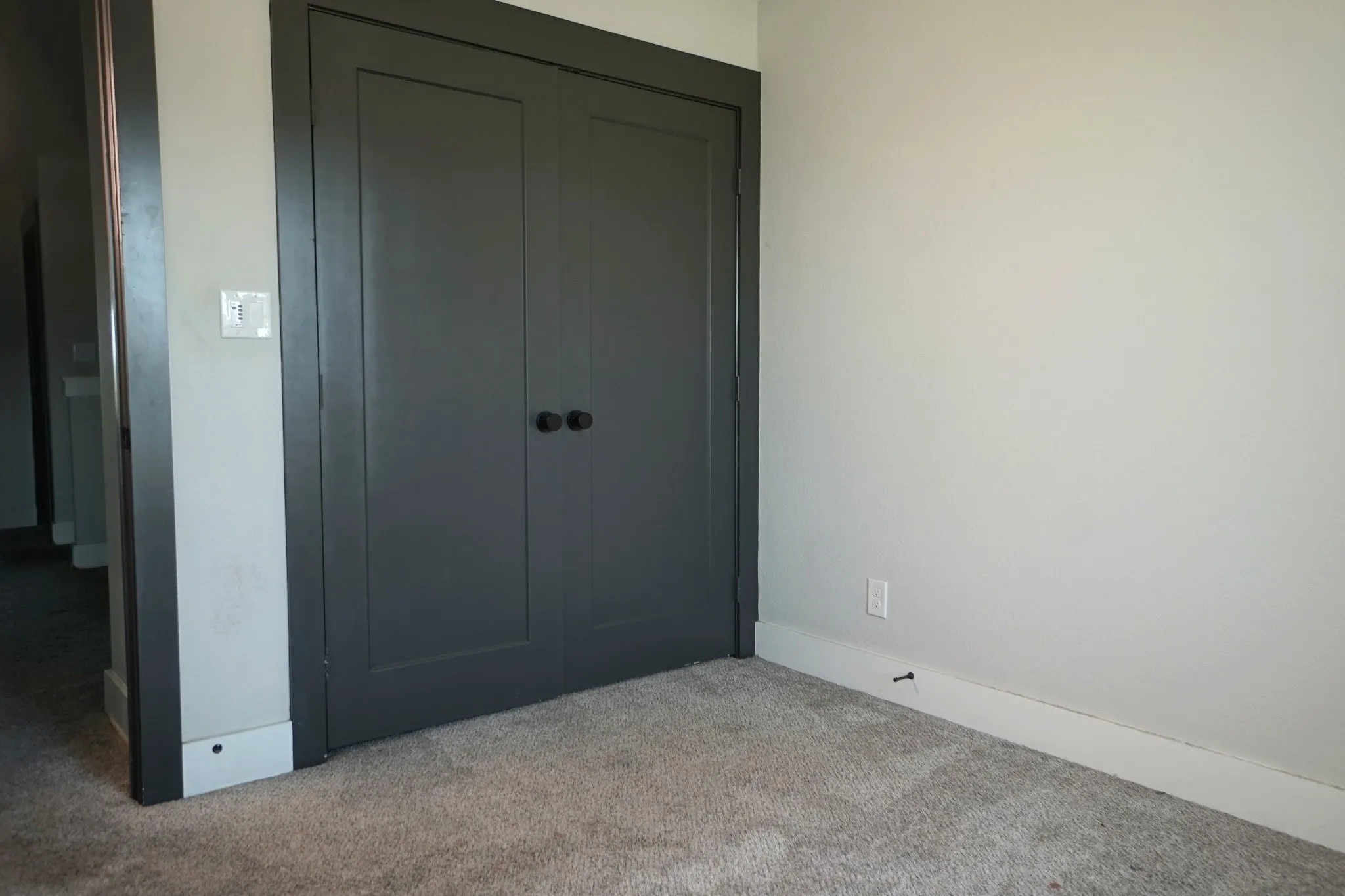 Gray paneled bi-fold closet doors with round black hardware, light gray walls, and light gray carpeting