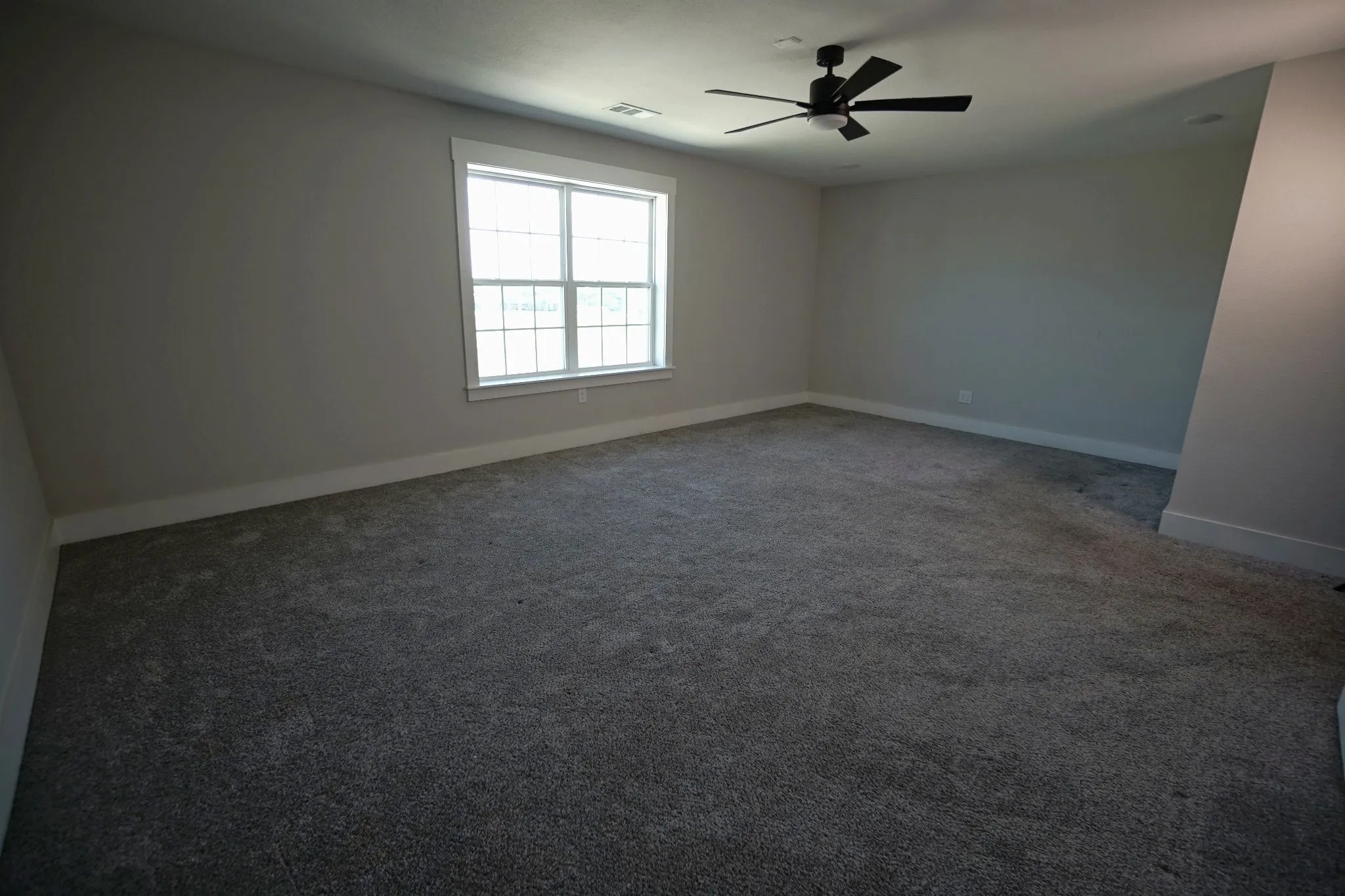 Spacious room with gray textured carpeting, a multi-pane window, and a ceiling fan with integrated lighting
