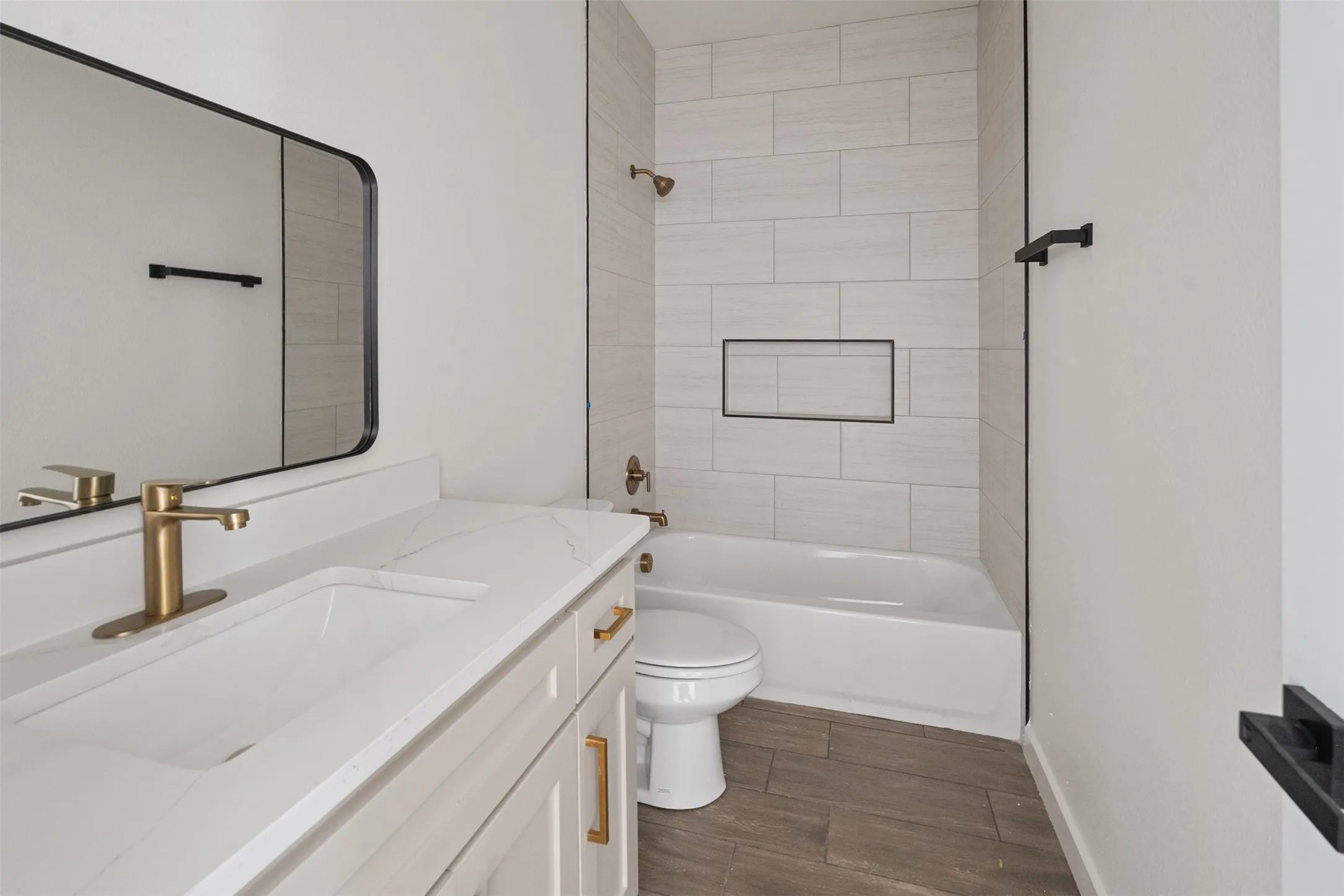 Bathroom featuring a rectangular undermount sink, a white countertop, gold-finish fixtures, and wood-finish flooring