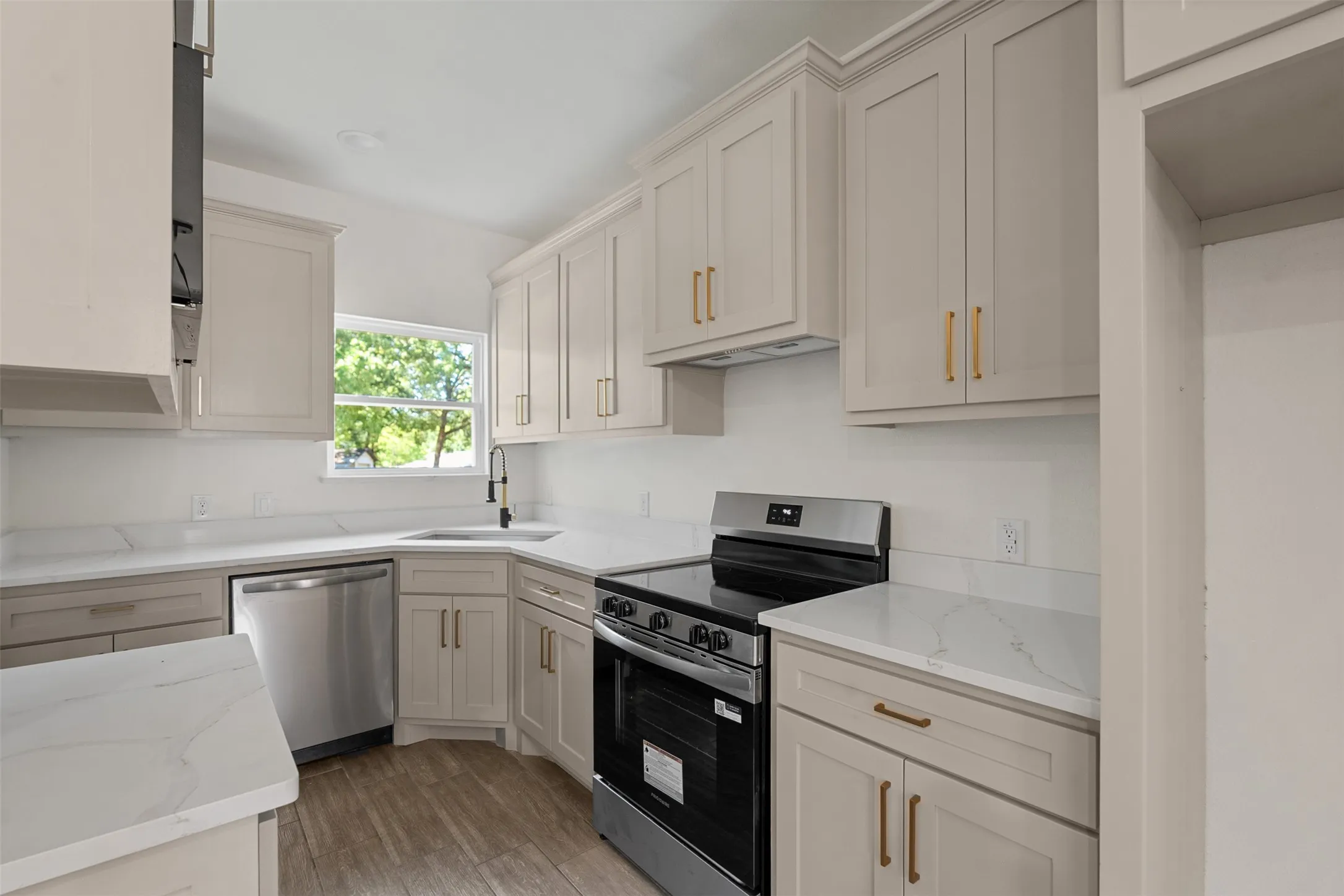 Contemporary kitchen featuring light wood-finish cabinetry, white countertops, stainless steel appliances, a corner sink with a gooseneck faucet, and wood-look flooring