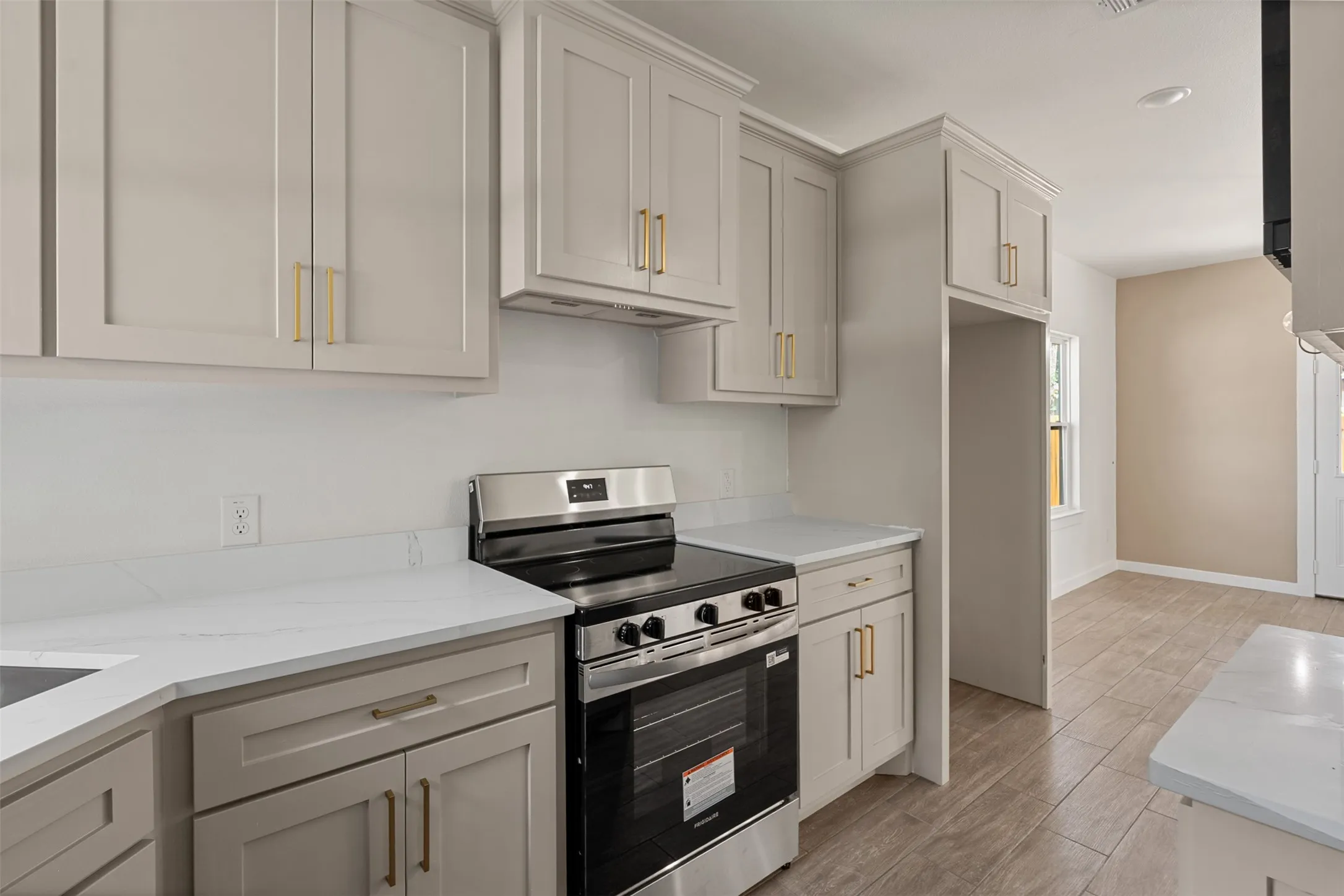 Kitchen featuring light-toned cabinetry with gold-toned hardware, white solid surface countertops, and a stainless steel electric range