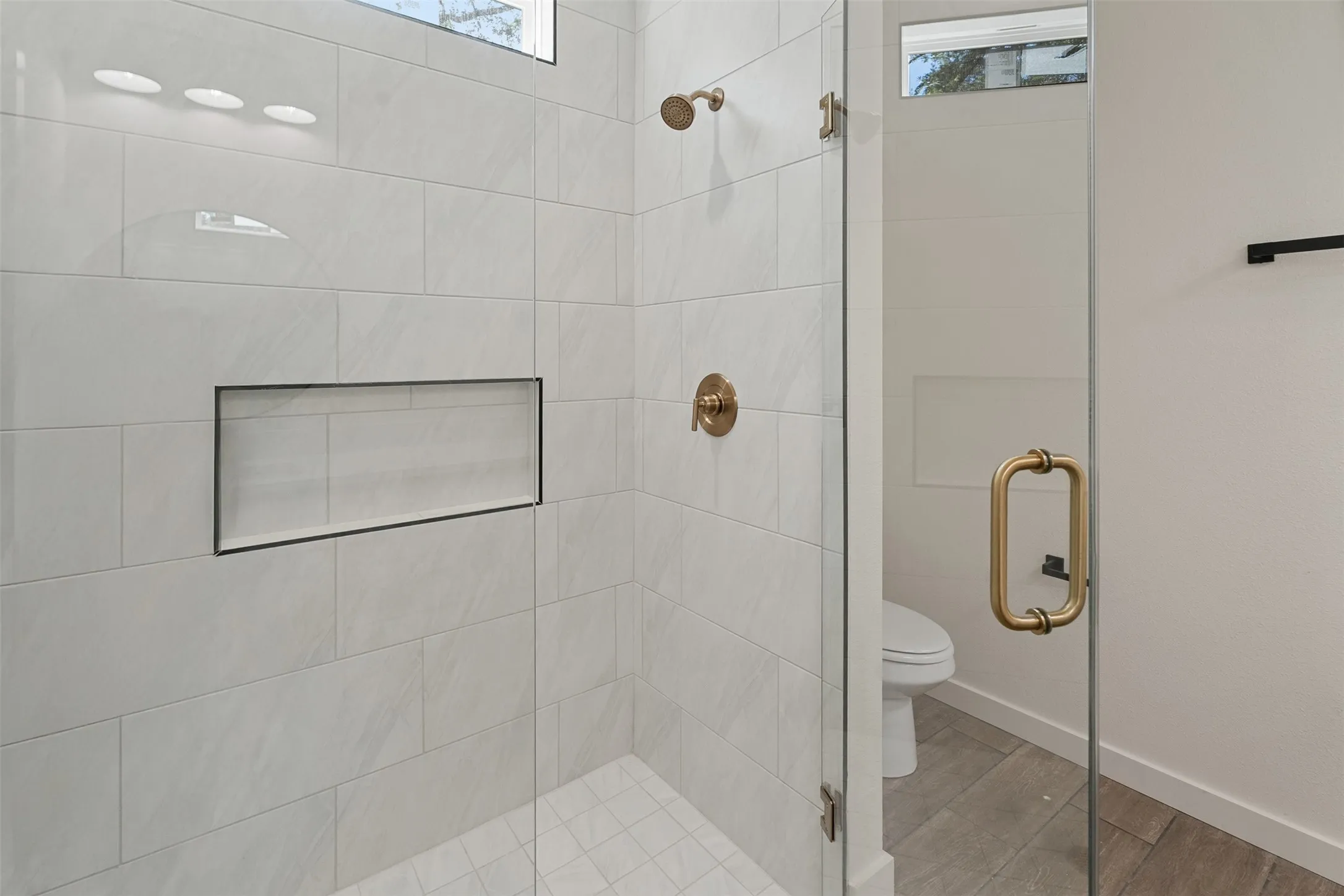 Walk-in shower featuring a frameless glass enclosure, white rectangular subway tile, integrated shower niche, and brass fixtures