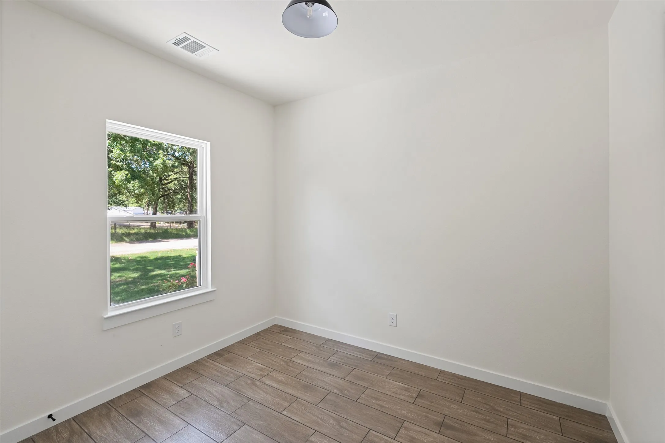 Room with light wood-finish flooring, white walls, and a single-pane window