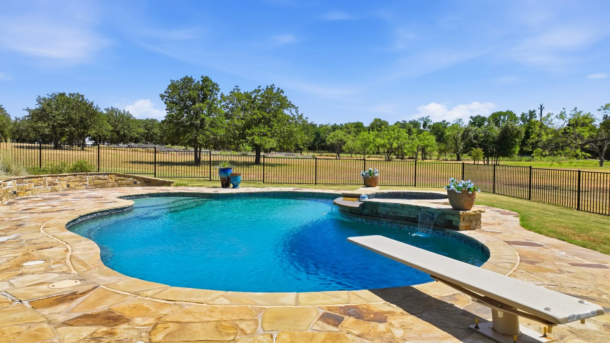 Curved swimming pool with a diving board, integrated spa with waterfall feature, and flagstone pool decking