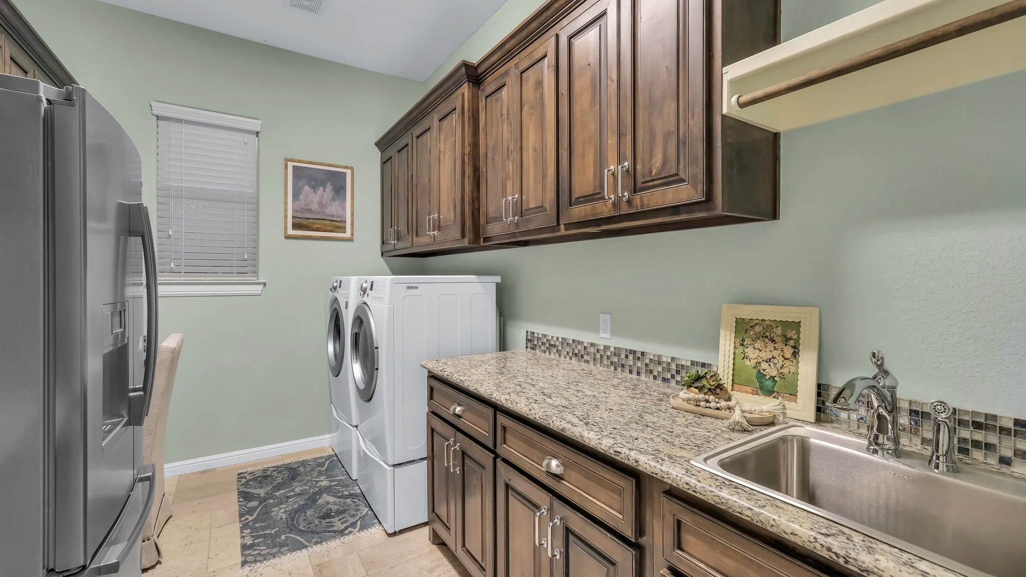 Utility room featuring extensive dark wood cabinetry, a granite-finish countertop with an undermount sink, and a mosaic tile backsplash