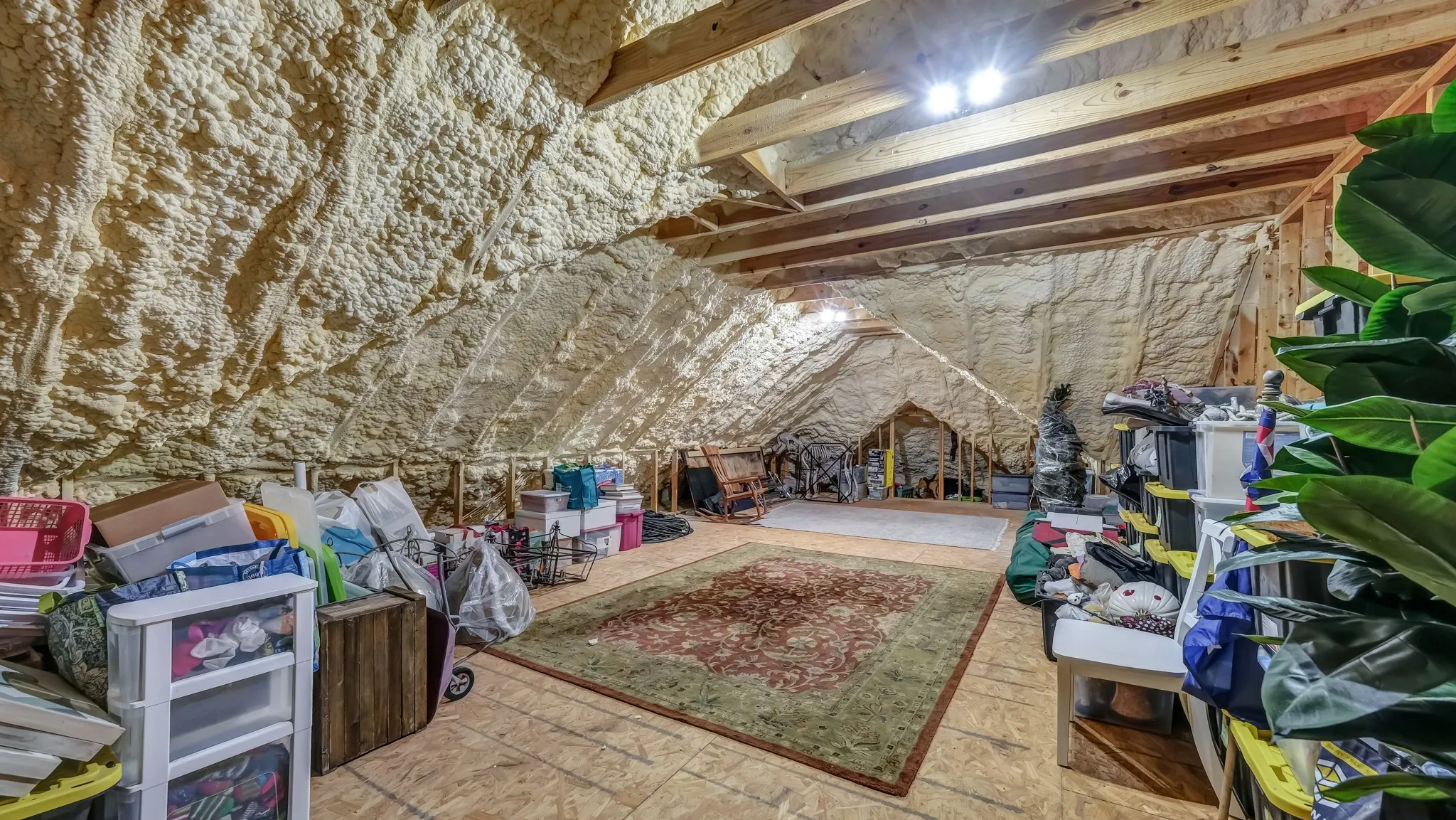 Spacious attic area featuring extensive spray foam insulation, exposed wood rafters, and plywood subflooring