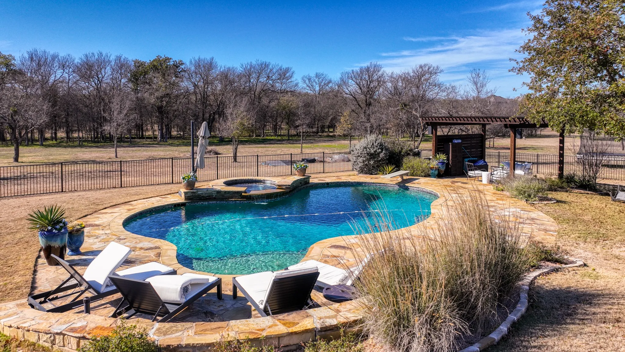 Kidney-shaped swimming pool featuring a stone surround, an integrated spa, and a diving board