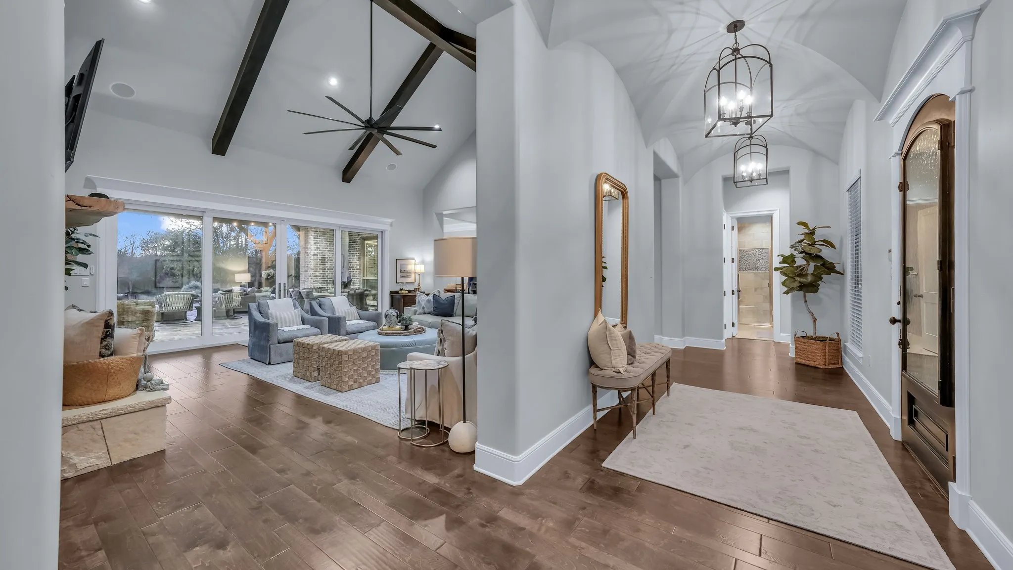 Vaulted living room with exposed wood beams, wood-finish flooring, and a stone fireplace