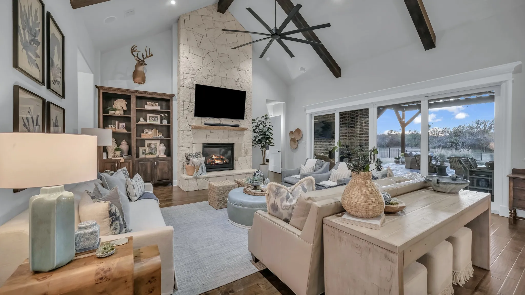Living area featuring a stone-clad fireplace, vaulted ceiling with exposed wood beams, wood-finish flooring, and expansive sliding glass doors leading to an outdoor space