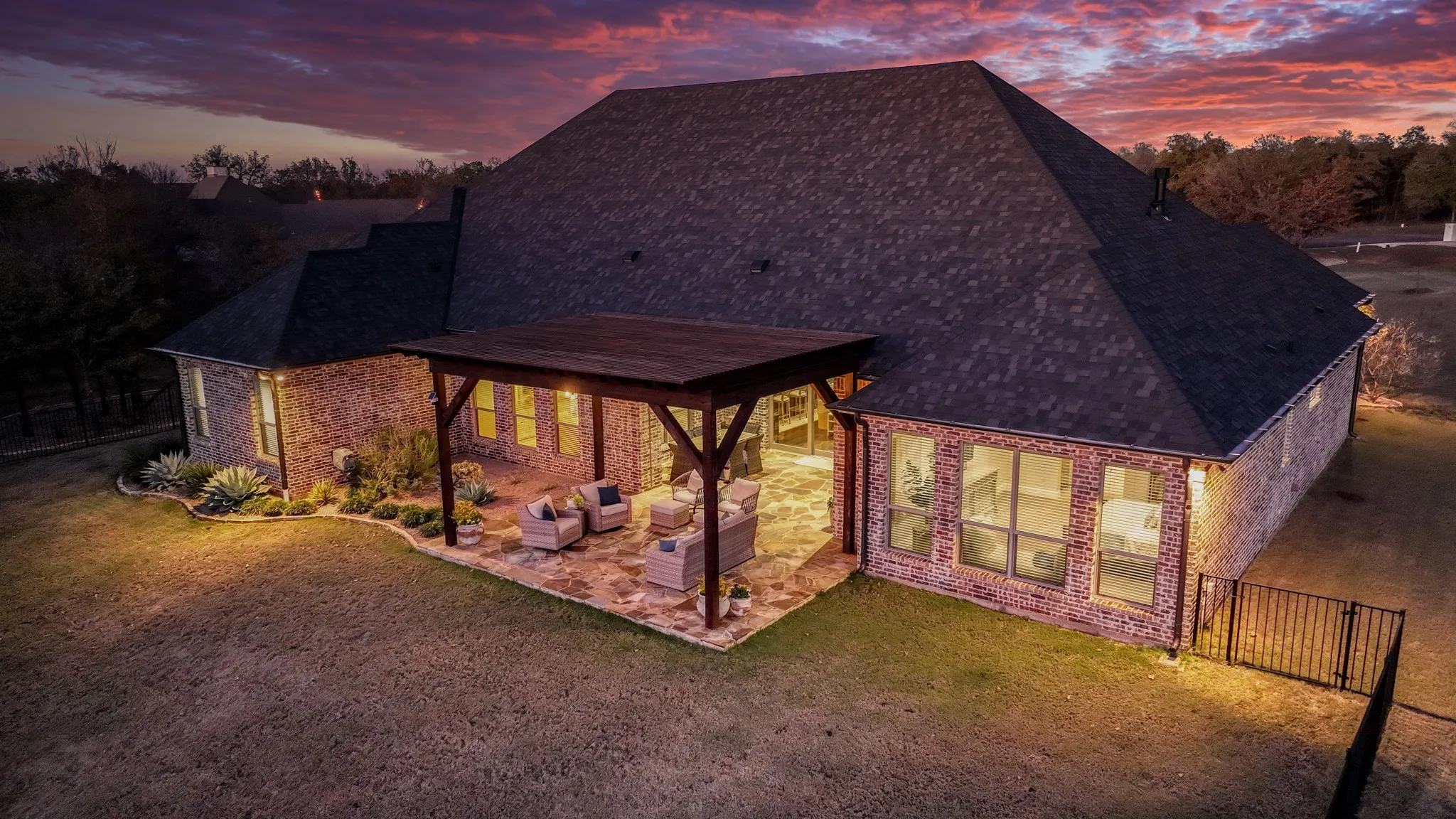 Brick exterior home featuring a covered patio with a wood pergola, stone patio flooring, and a landscaped perimeter