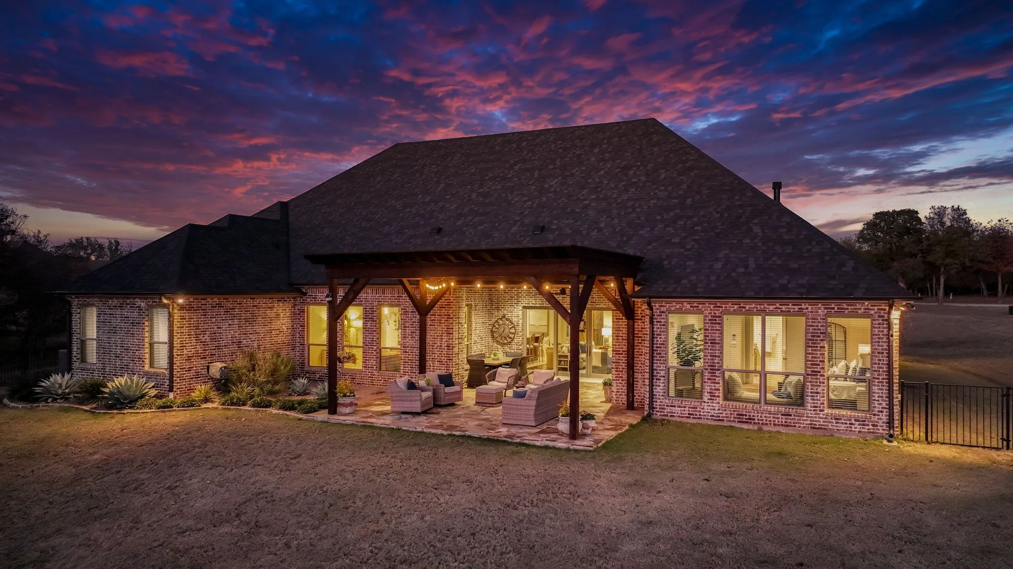 Expansive backyard featuring a stone patio, a large wooden pergola, and brick exterior