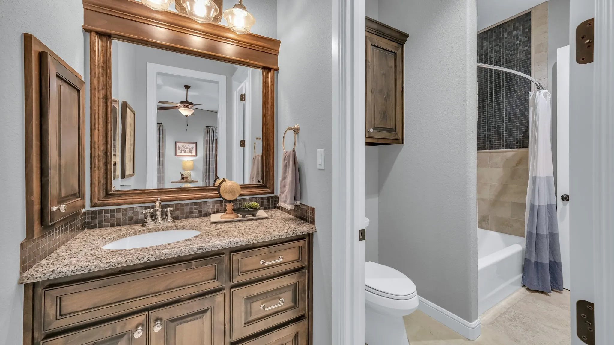 Bathroom vanity featuring a light-toned granite countertop with an undermount sink, mosaic tile backsplash, and dark wood-finish cabinetry
