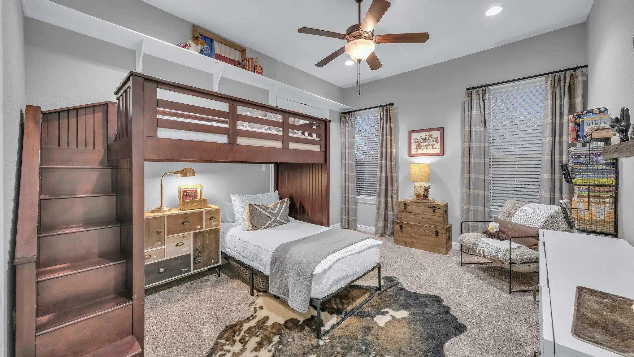 Spacious room featuring a built-in wooden bunk bed with integrated stairs, neutral carpeting, and a ceiling fan with light fixture
