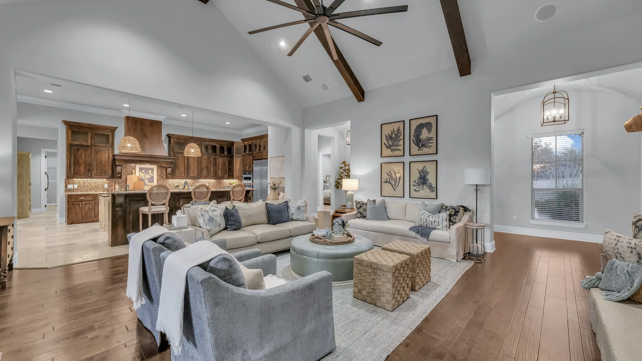 Spacious living area featuring high vaulted ceilings with exposed wood beams, wood-finish flooring, and a kitchen visible through a wide arched entry