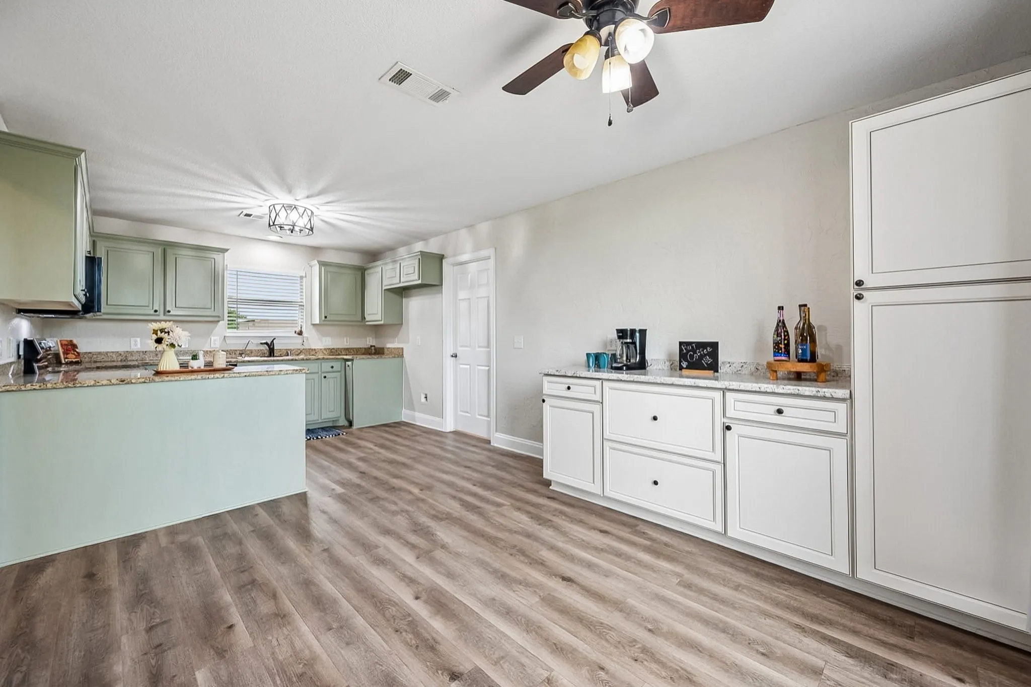Kitchen featuring mint green cabinetry, granite countertops, wood-finish flooring, a breakfast bar, and an additional white cabinet and counter area