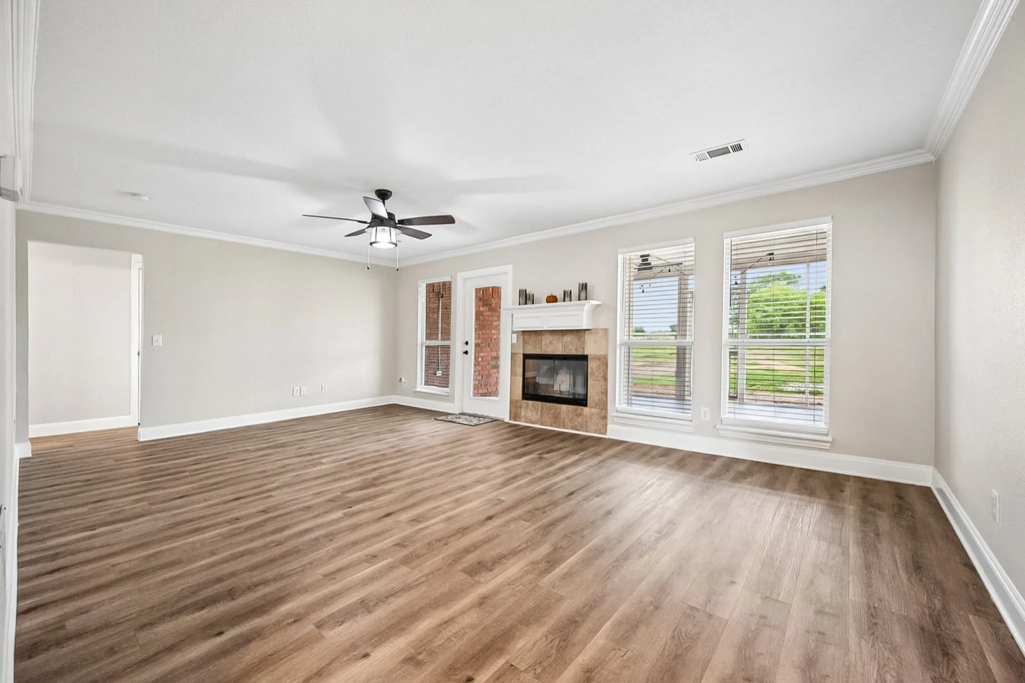 Spacious living area featuring wood-finish flooring, a ceiling fan with integrated lighting, and multiple windows with blinds