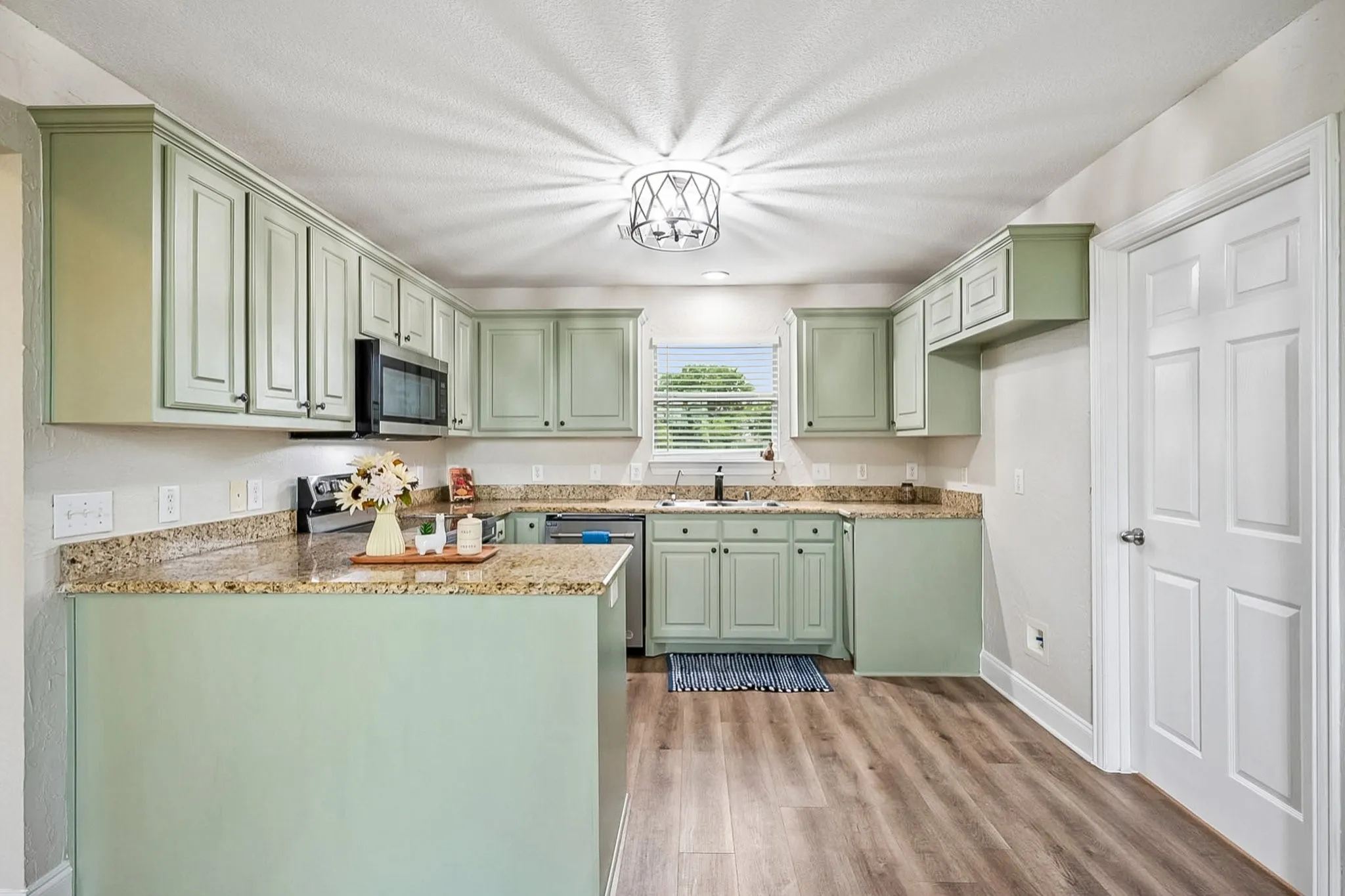 Kitchen featuring light green cabinetry, granite countertops, stainless steel appliances, wood-finish flooring, and a contemporary ceiling light fixture