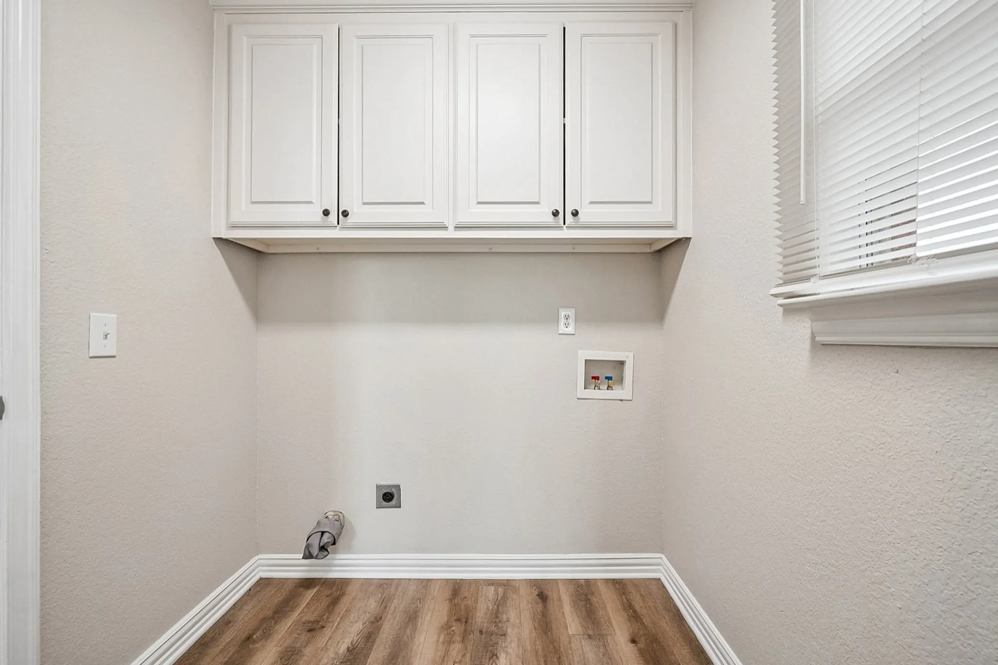 Laundry area featuring wood-finish flooring, white baseboards, and white upper cabinetry