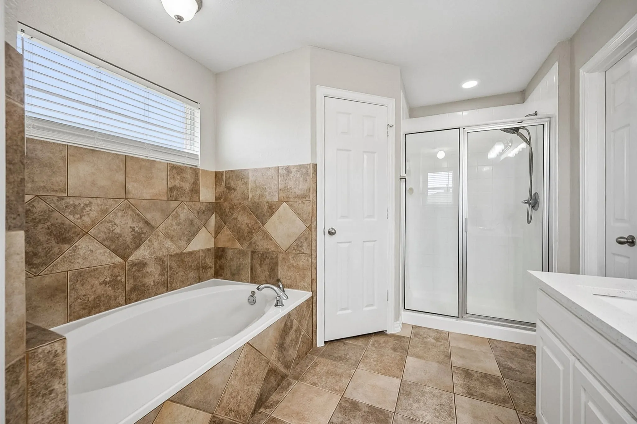Bathroom featuring a built-in soaking tub with a tile surround, a separate glass-enclosed shower, and a single vanity with a white countertop