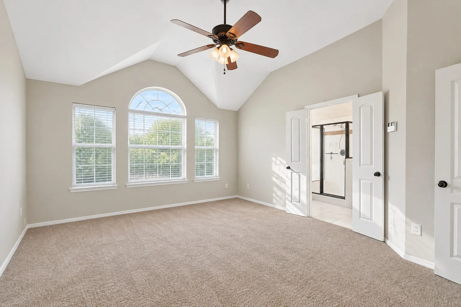 Vaulted ceiling with a ceiling fan, arched window, two rectangular windows with blinds, and carpet flooring
