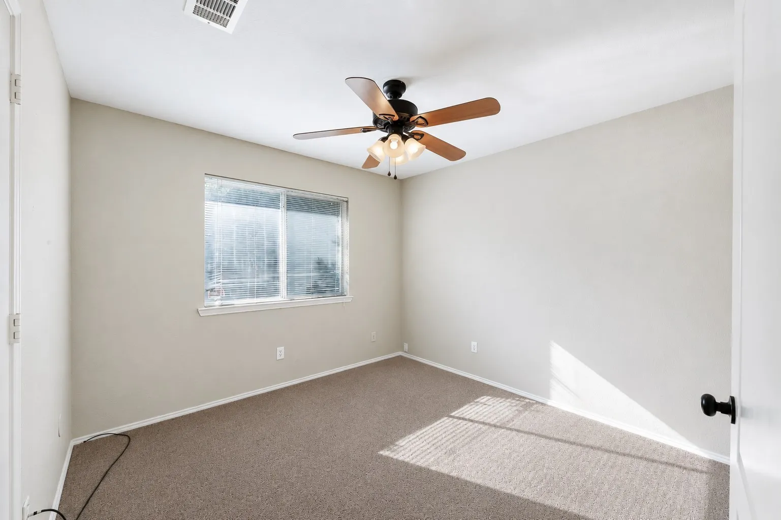 Room featuring neutral-toned carpet, a ceiling fan with wood-finish blades, and a window with blinds