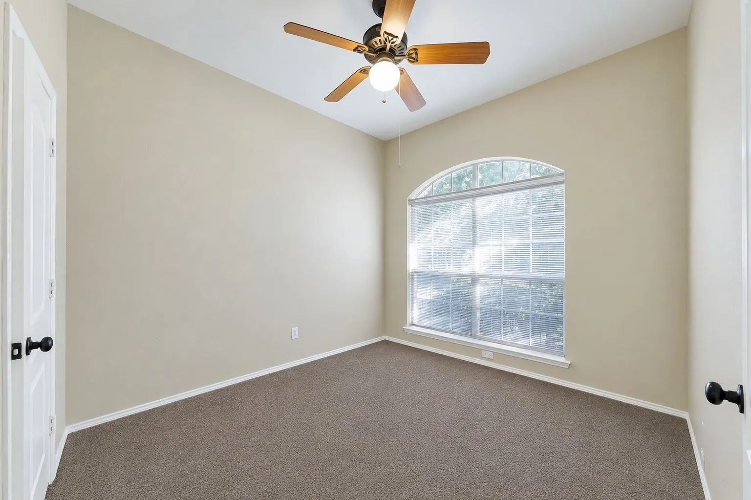 Room featuring an arched window, a ceiling fan with light fixture, neutral-toned walls, and carpet flooring