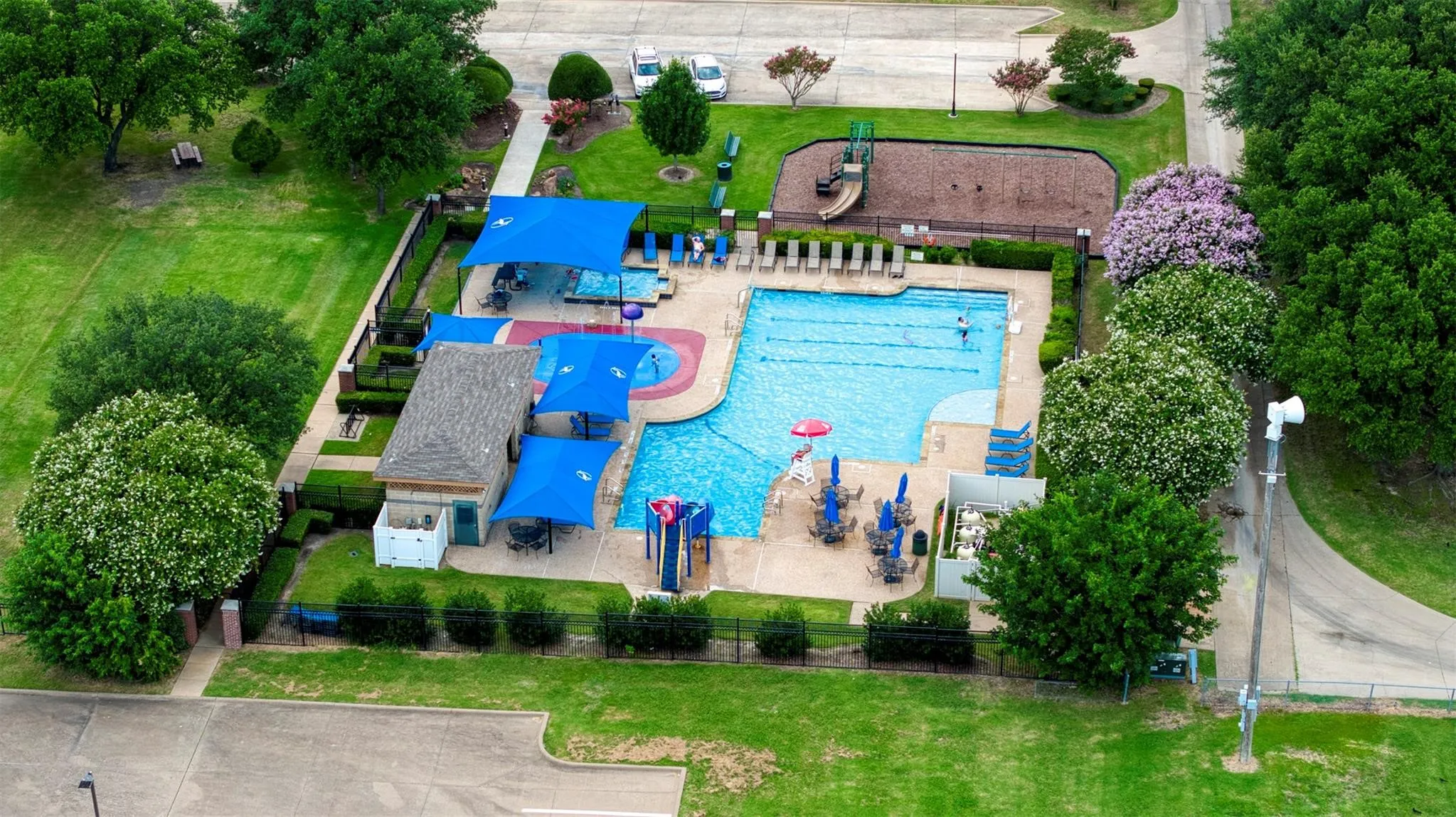 Community swimming pool featuring, a separate children's splash pad, and multiple shaded lounge areas