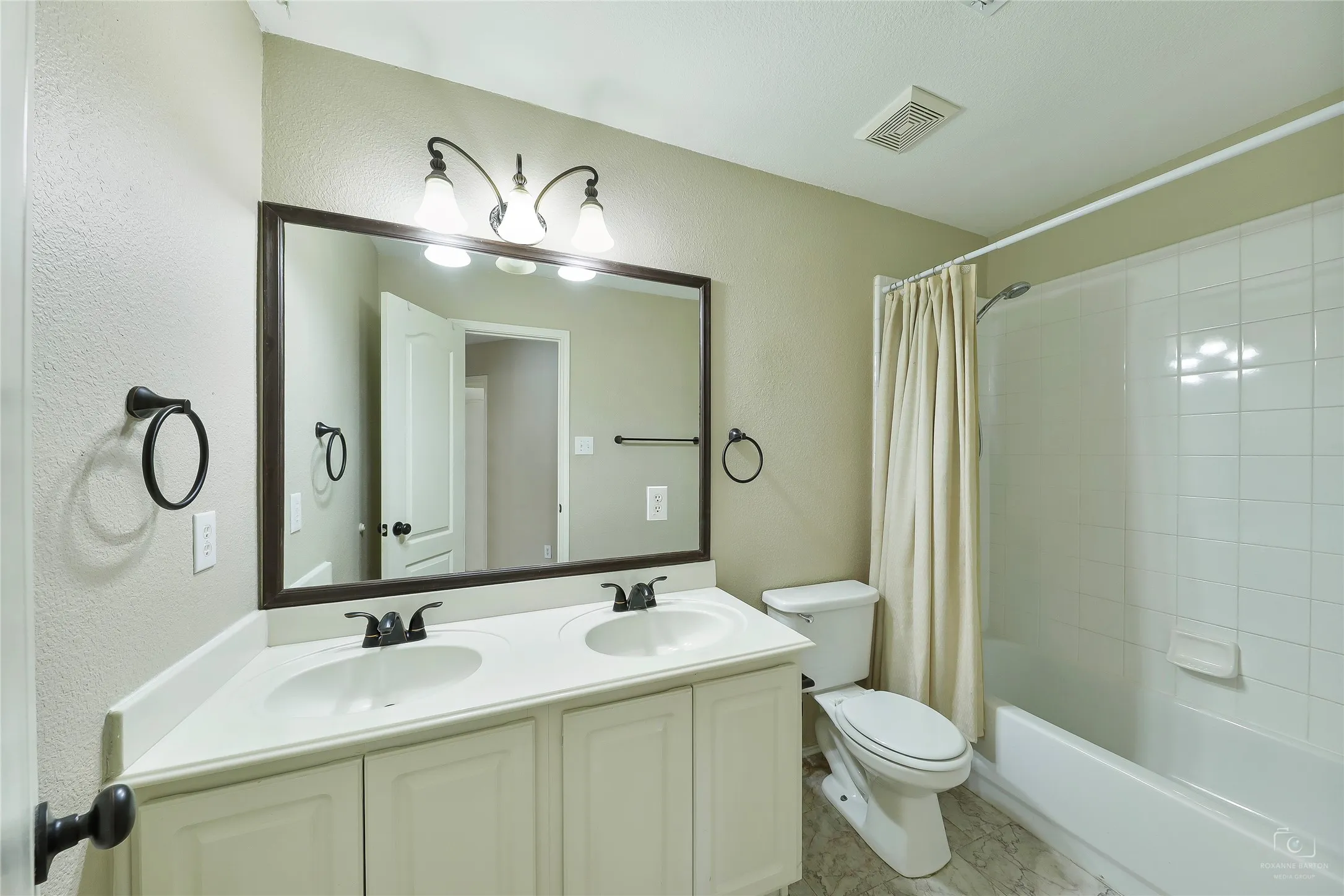 Bathroom featuring a dual vanity with white cabinetry, a large framed mirror, and a full bathtub with white tile surround