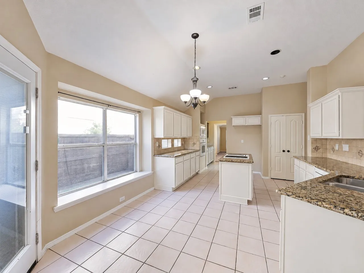 Kitchen featuring tile flooring, white cabinetry, granite countertops, a center island with a cooktop, and a double-basin sink