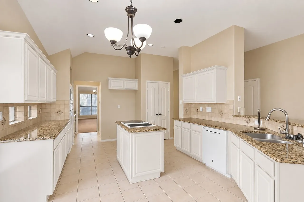 Kitchen featuring white cabinetry, granite countertops, tile flooring, a center island, and a dual basin sink