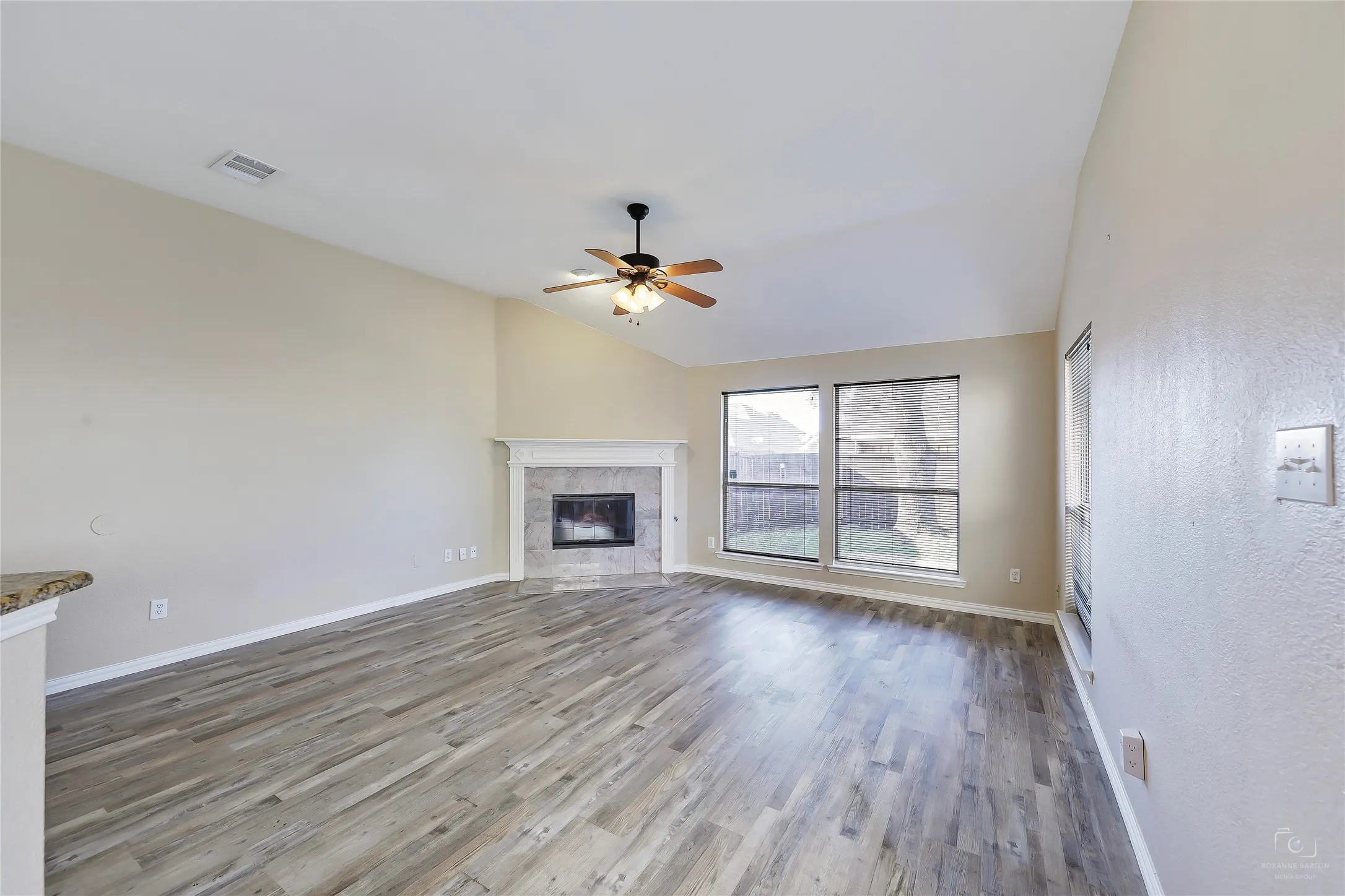 Living area featuring vaulted ceilings, wood-finish flooring, and a corner fireplace with a decorative mantel and stone surround