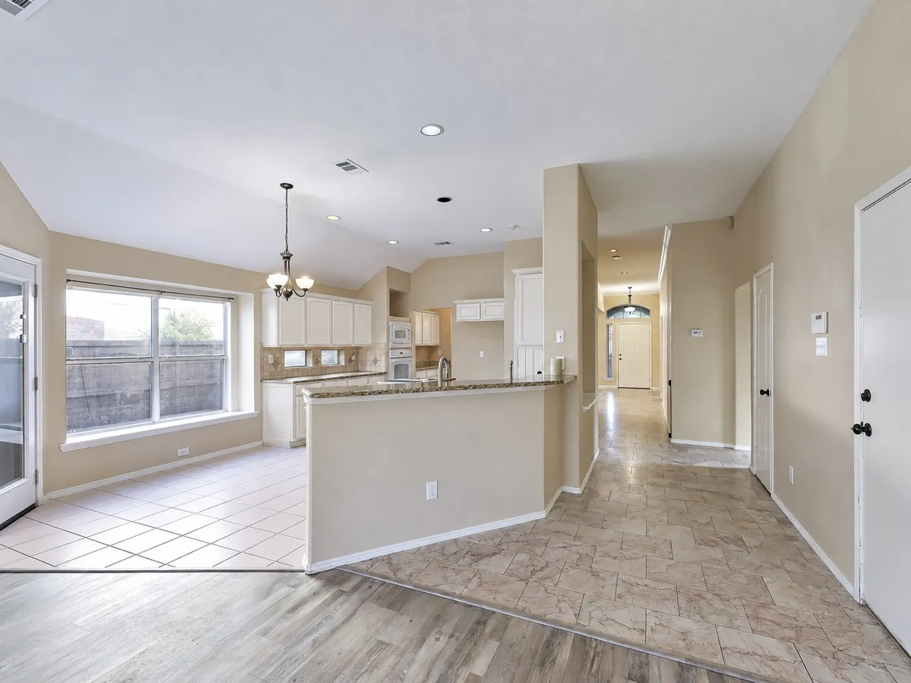 Open-concept design featuring a kitchen with white cabinetry and a breakfast bar, a dining area with a chandelier, and a hallway leading to the front entry