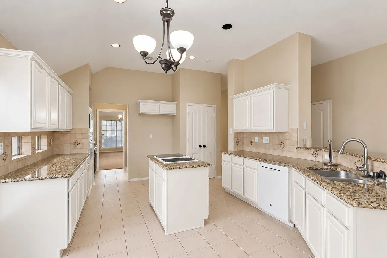 Spacious kitchen featuring white cabinetry, granite countertops, a center island with cooktop, stainless steel appliances, pendant lighting, and neutral tile flooring throughout the open layout