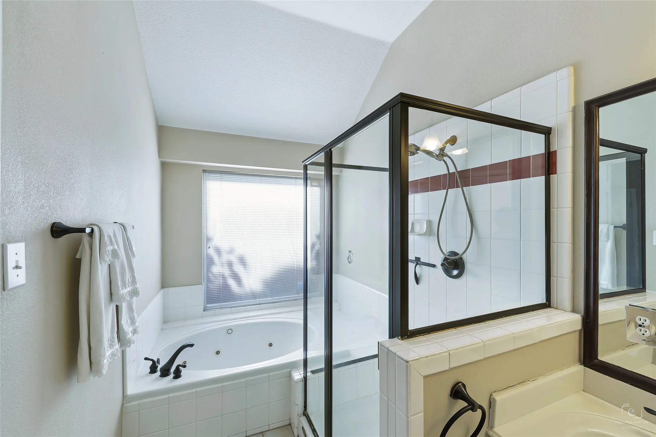 Bathroom featuring a jetted tub, enclosed shower with a glass panel, and a vanity with a framed mirror