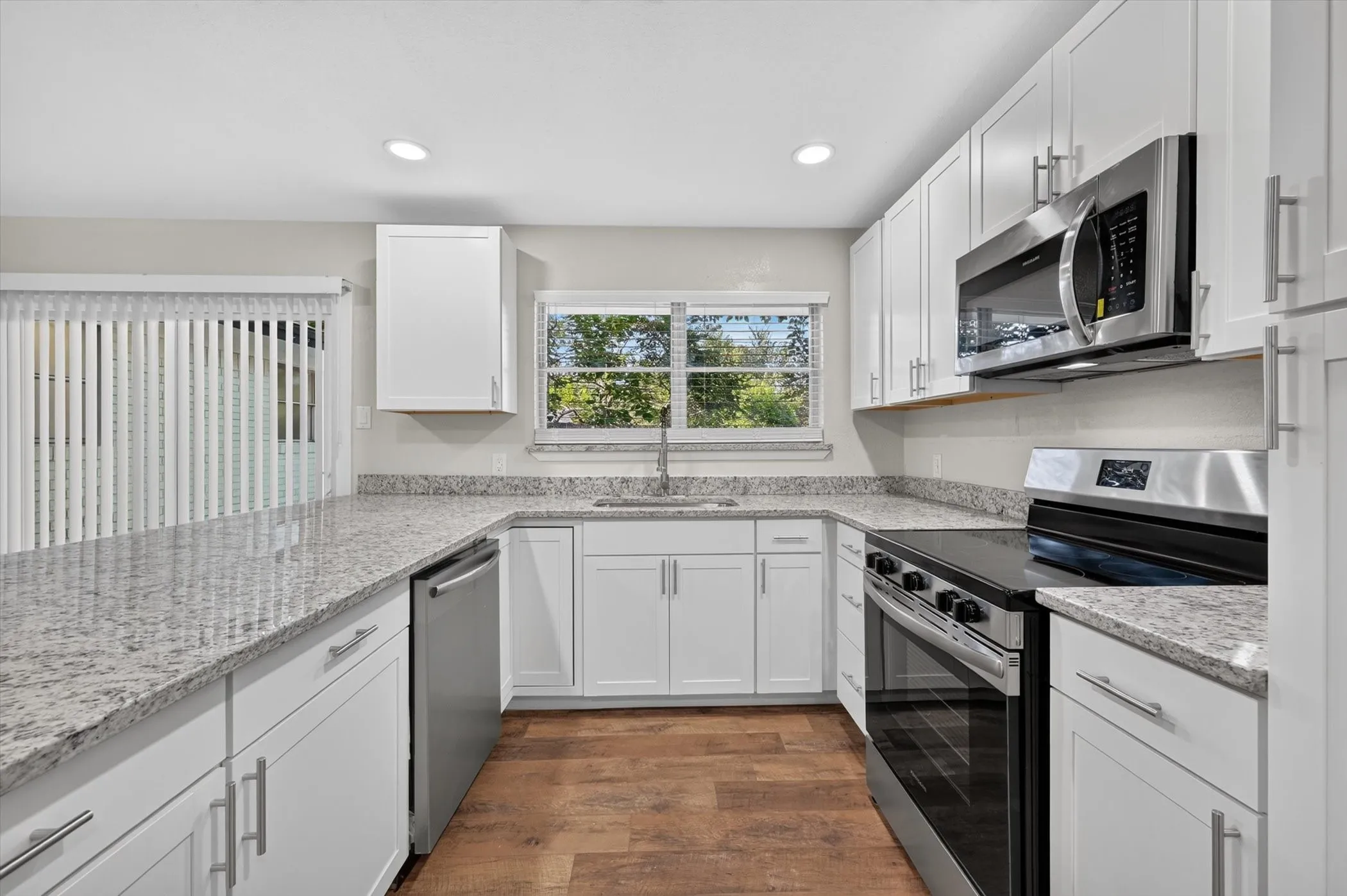 Kitchen featuring white cabinetry, light-toned countertops, stainless steel appliances, wood-finish flooring, and recessed lighting