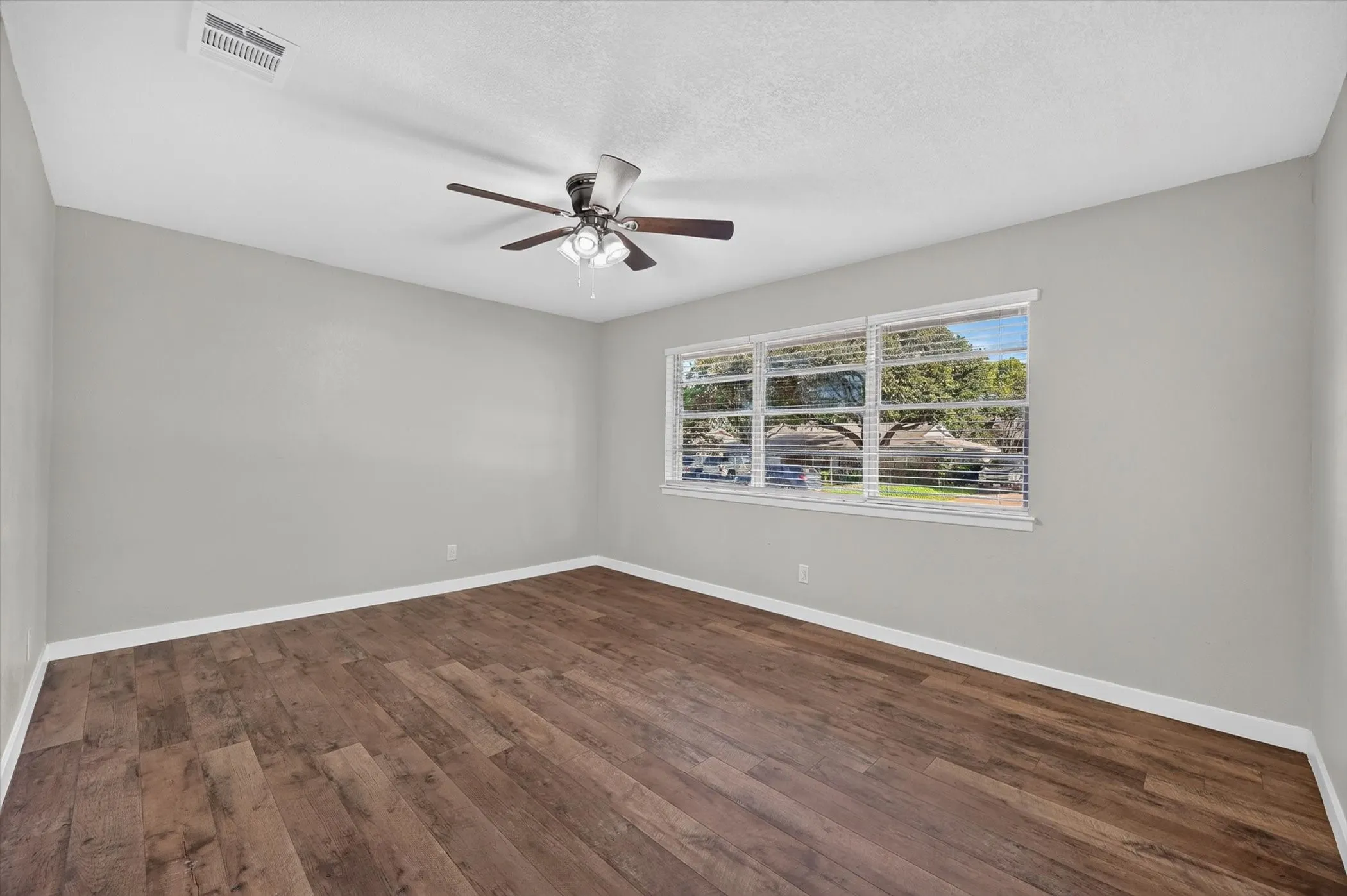 Spacious room featuring wood-finish flooring, light gray wall tones, and white trim