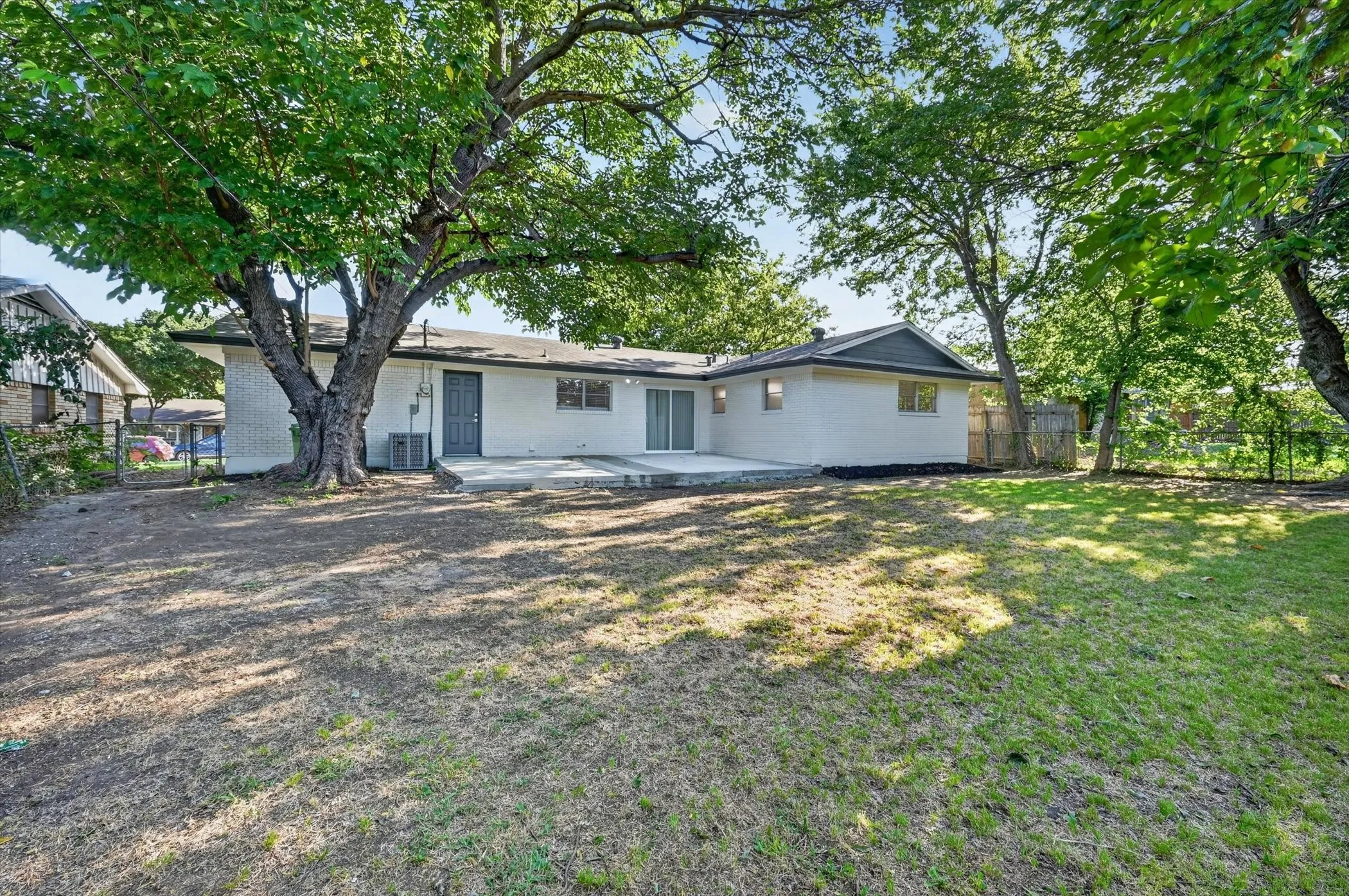 Spacious backyard with mature shade trees, a concrete patio, and a white brick exterior