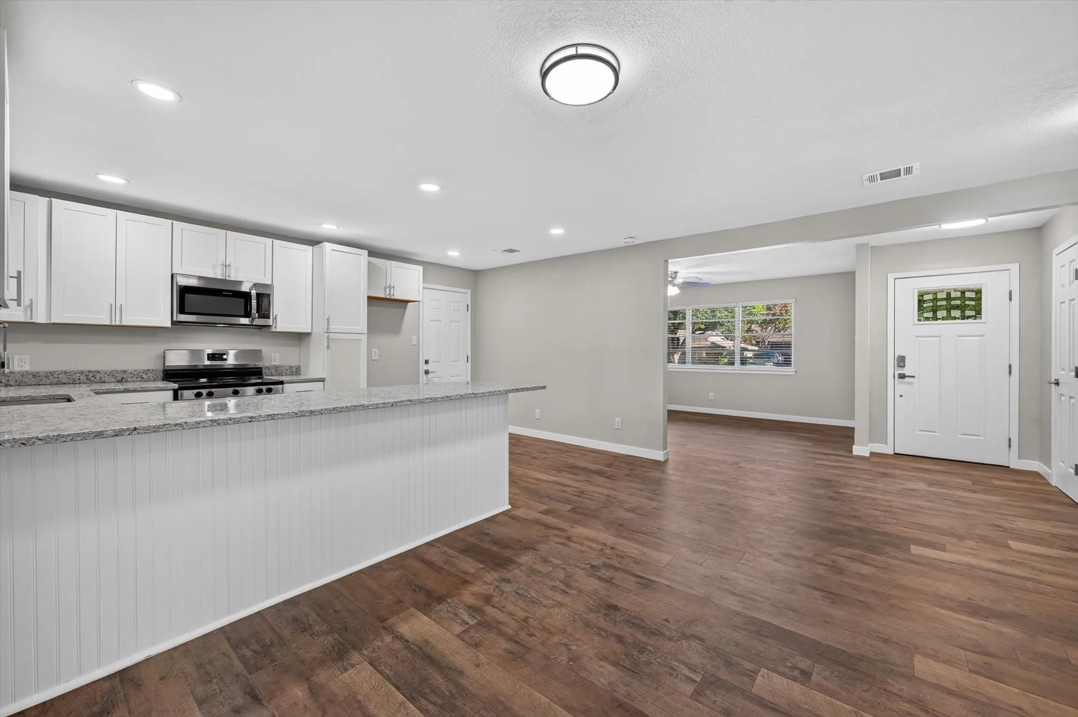 Kitchen featuring white cabinetry, granite countertops, stainless steel appliances, and a beadboard-paneled island