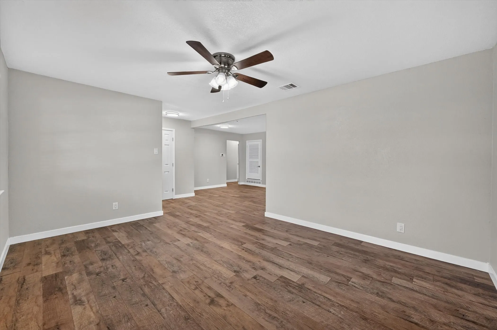 Spacious room featuring wood-finish flooring, light gray walls, and a ceiling fan with integrated lighting