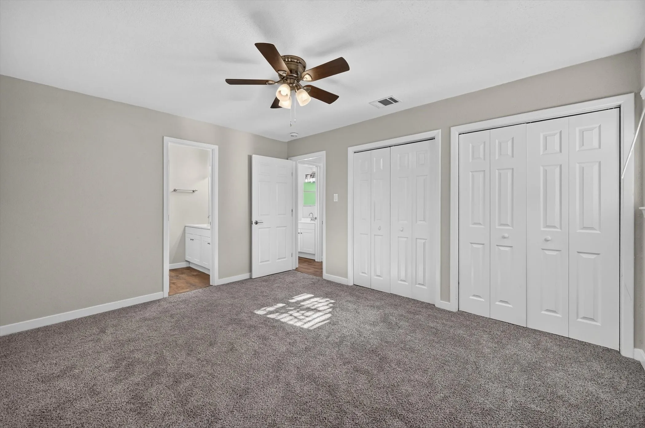 Carpeted room with light gray walls, two sets of bi-fold closet doors, a ceiling fan with integrated lighting, and two interior doorways
