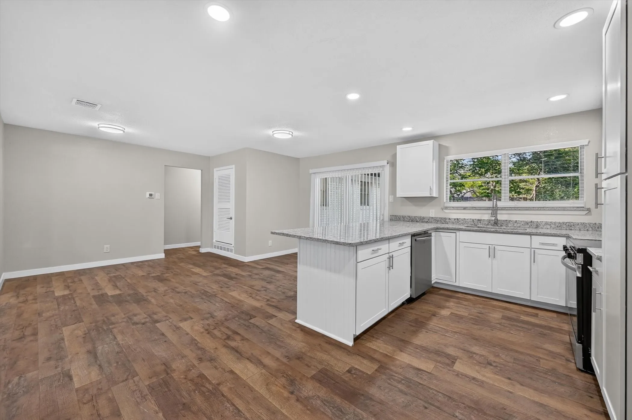 Open-concept kitchen and living area featuring wood-finish flooring, recessed lighting, and a kitchen island with stone countertops