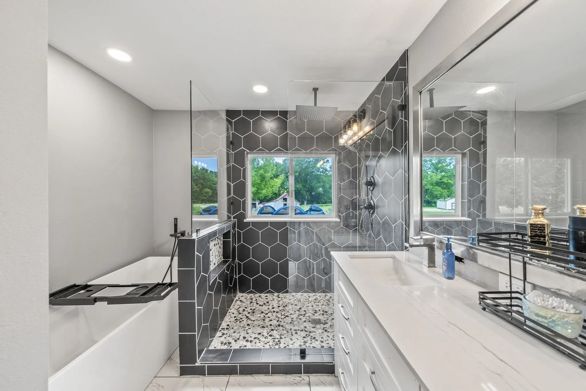 Contemporary bathroom featuring a hex-tiled shower with a rainfall showerhead, a large soaking tub with a floor-mounted faucet, and a dual-sink vanity with a solid surface countertop