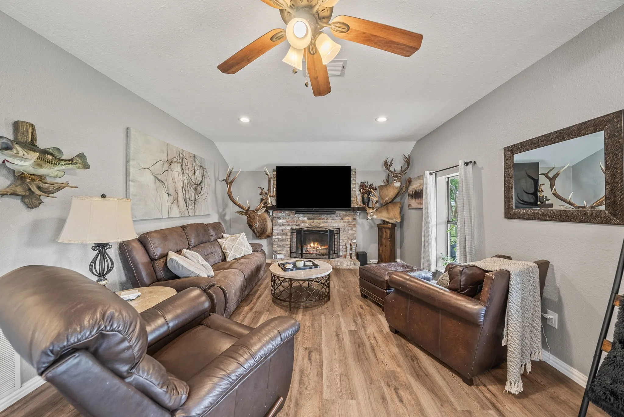 Living area featuring wood-finish flooring, a stone-faced fireplace, a vaulted ceiling with a ceiling fan, recessed lighting, and a glass-paneled exterior door