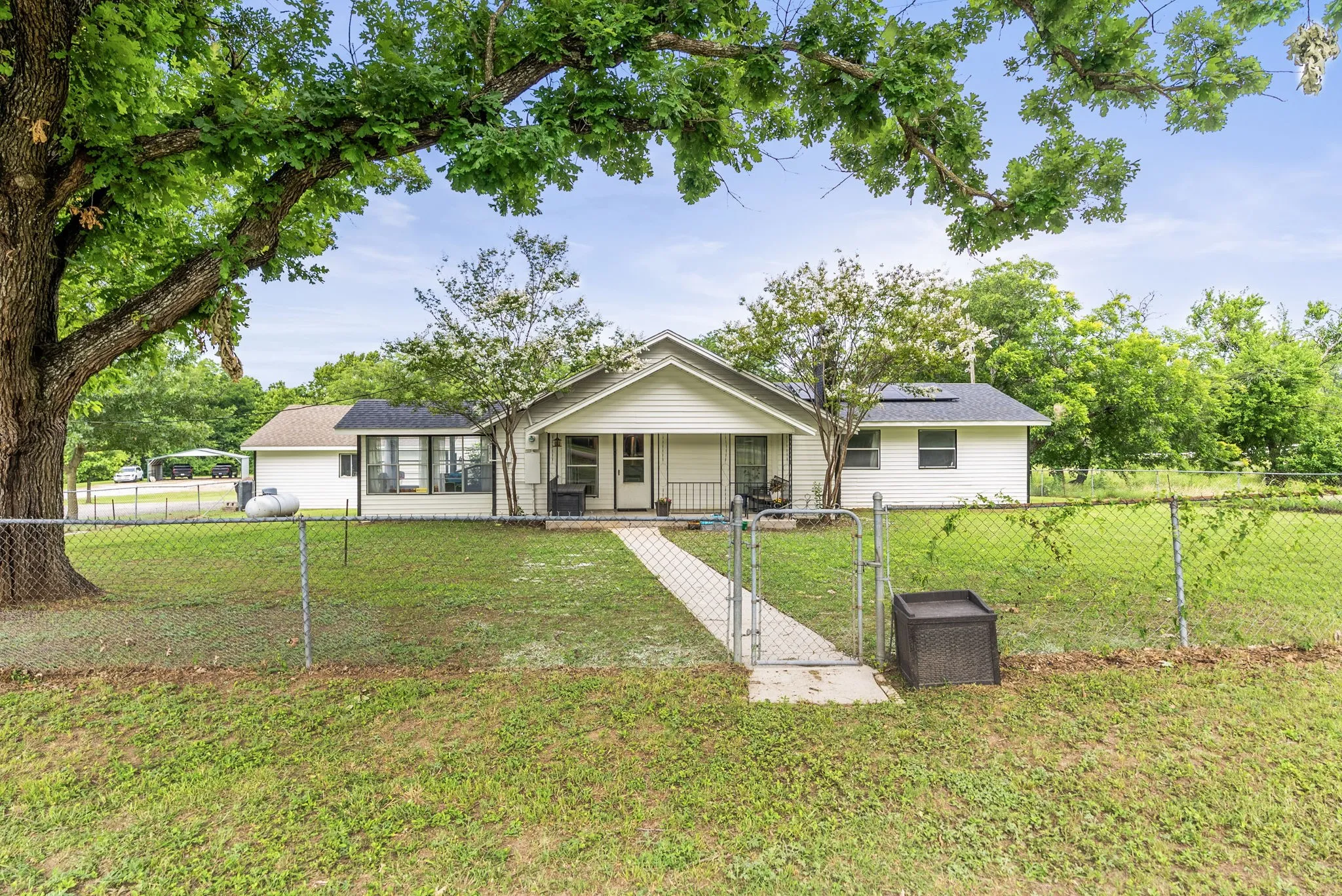 White-sided residence featuring a covered front porch and a chain-link fence enclosing the front yard