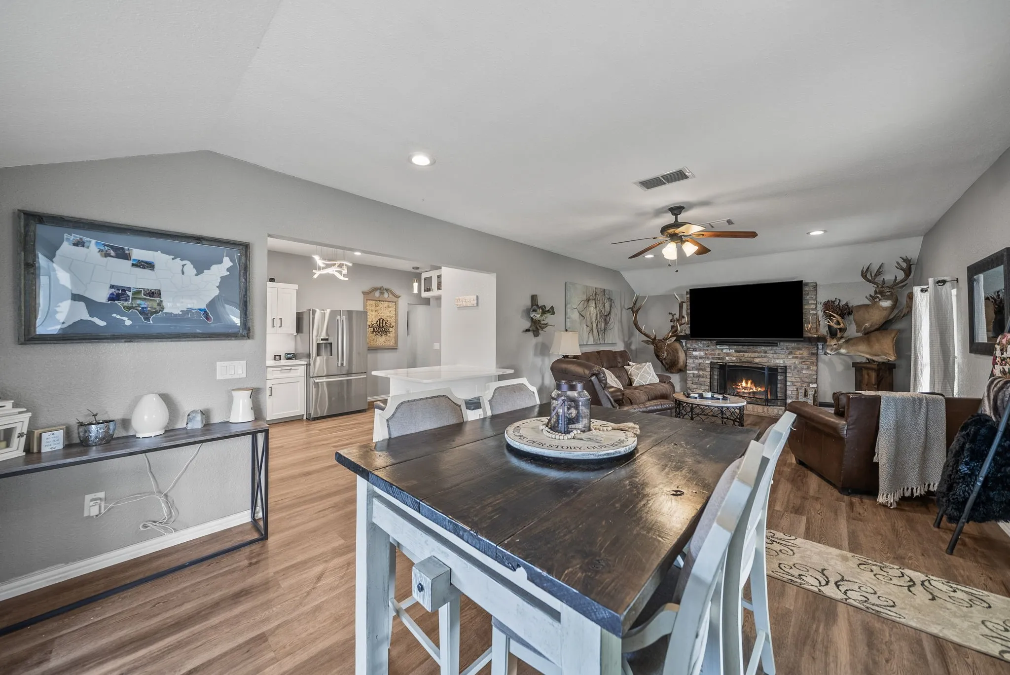 Open-concept living area featuring wood-finish flooring, a brick-surround fireplace, and a ceiling fan